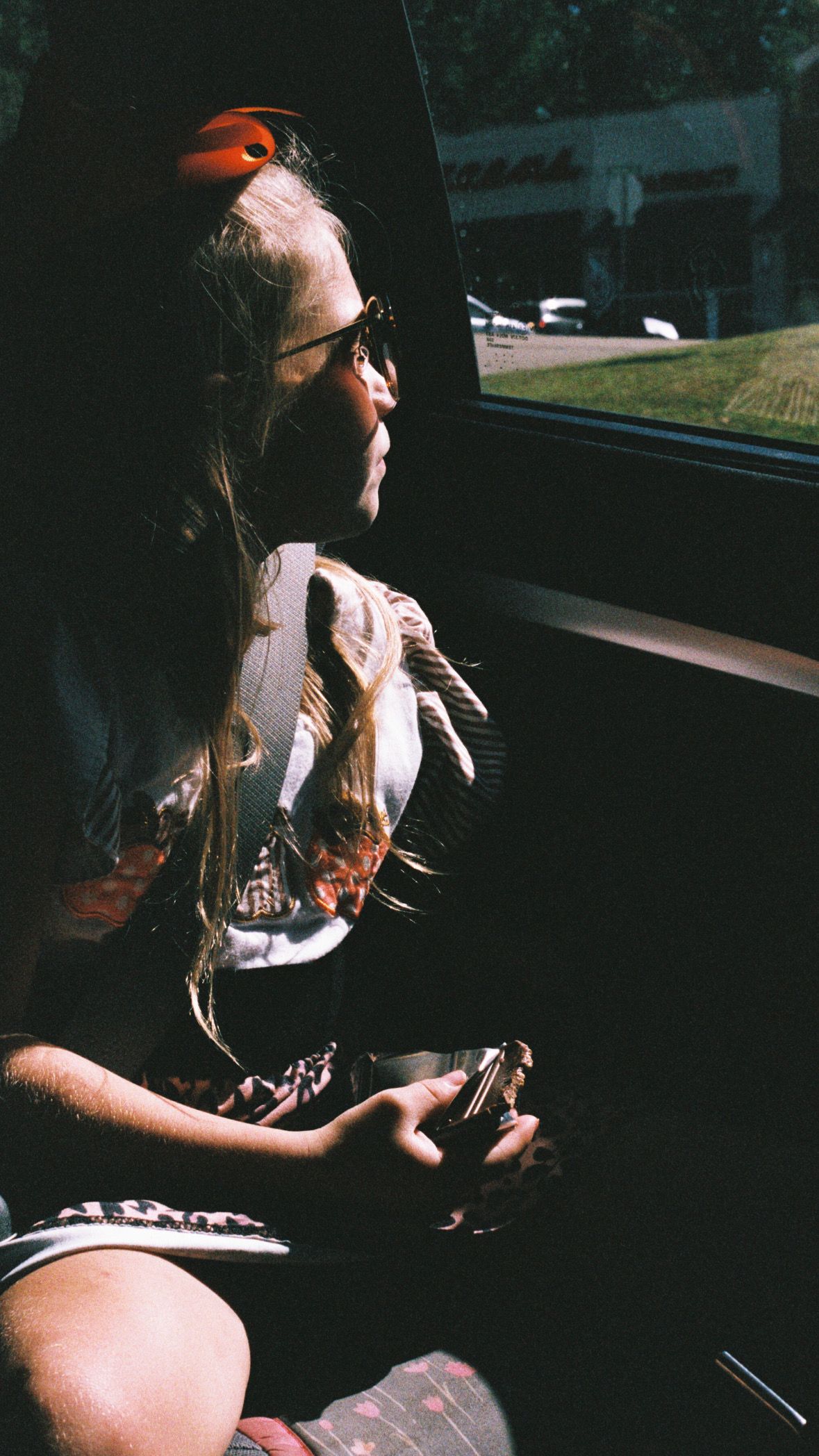Person sitting in a car holding a camera with sunlight streaming through the window.