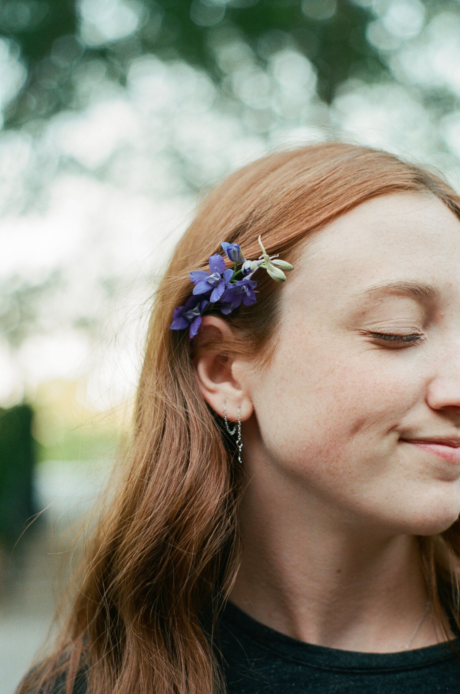 Close-up portrait with delicate purple flowers adorning long hair against blurred nature background.