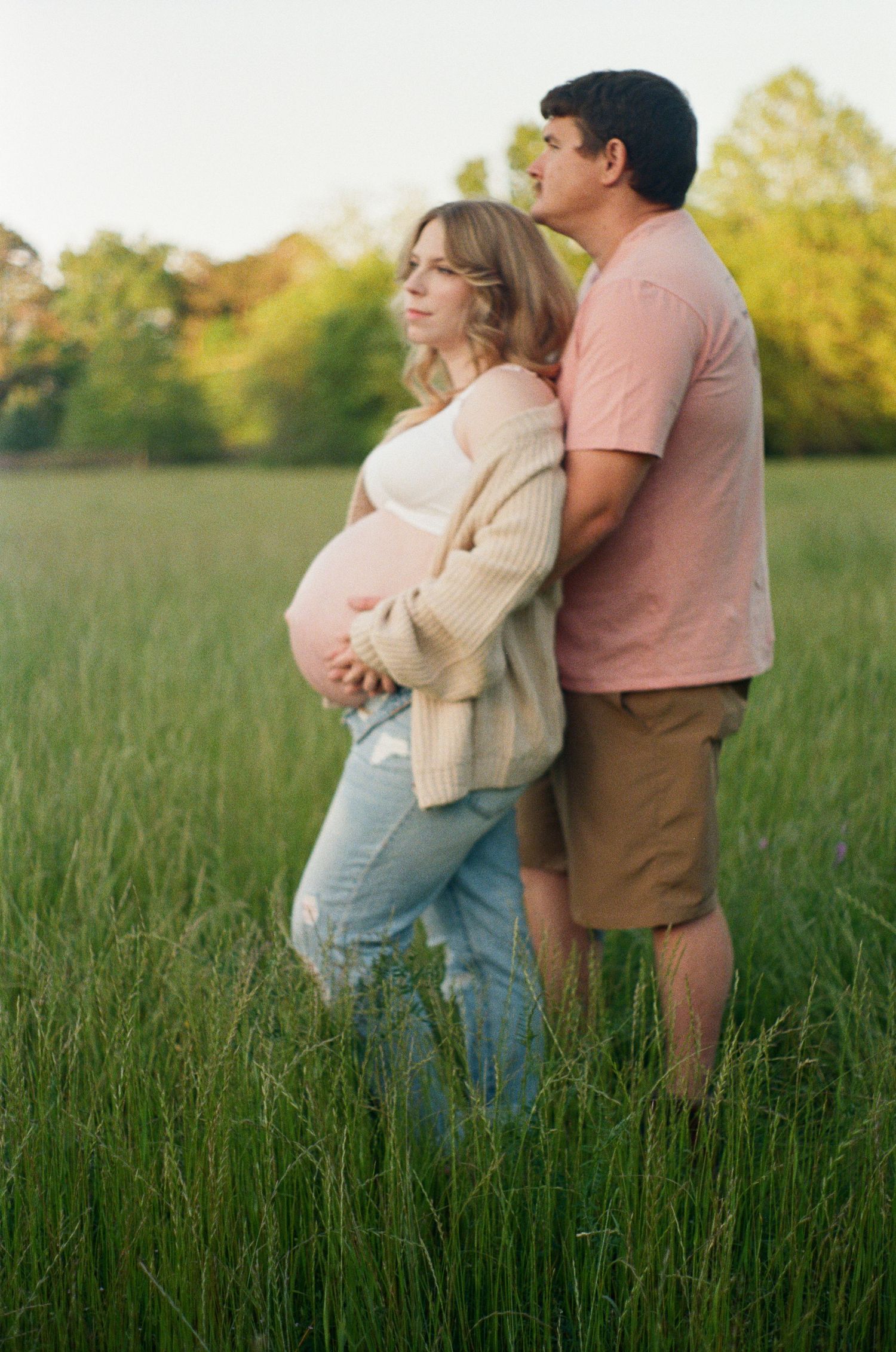 Romantic couple embraces in a sunlit meadow with tall grass during golden hour.