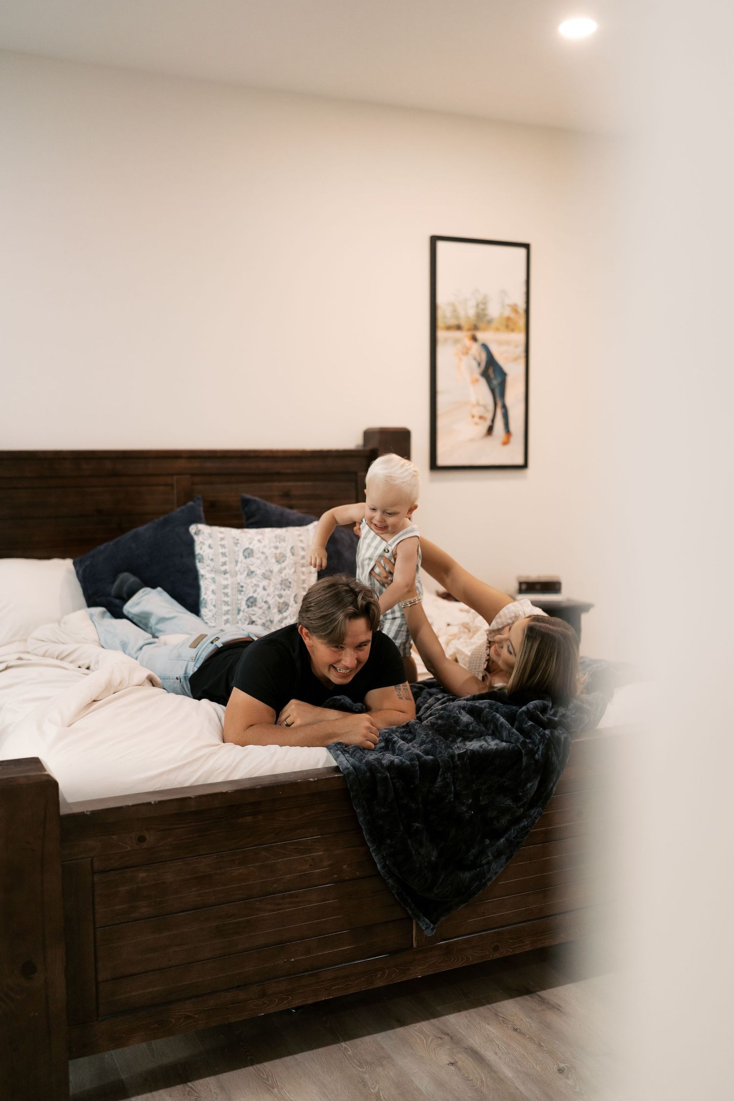 Family relaxing together on a dark wooden bed with a black blanket.
