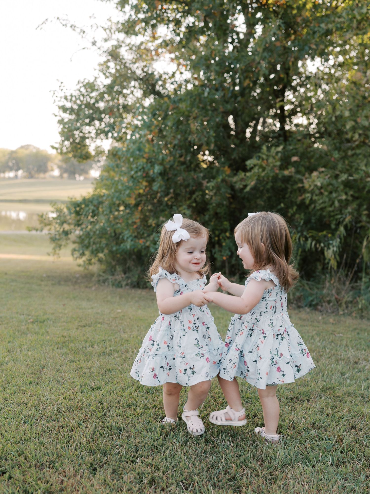 Two children in matching floral dresses playing together on grass.
