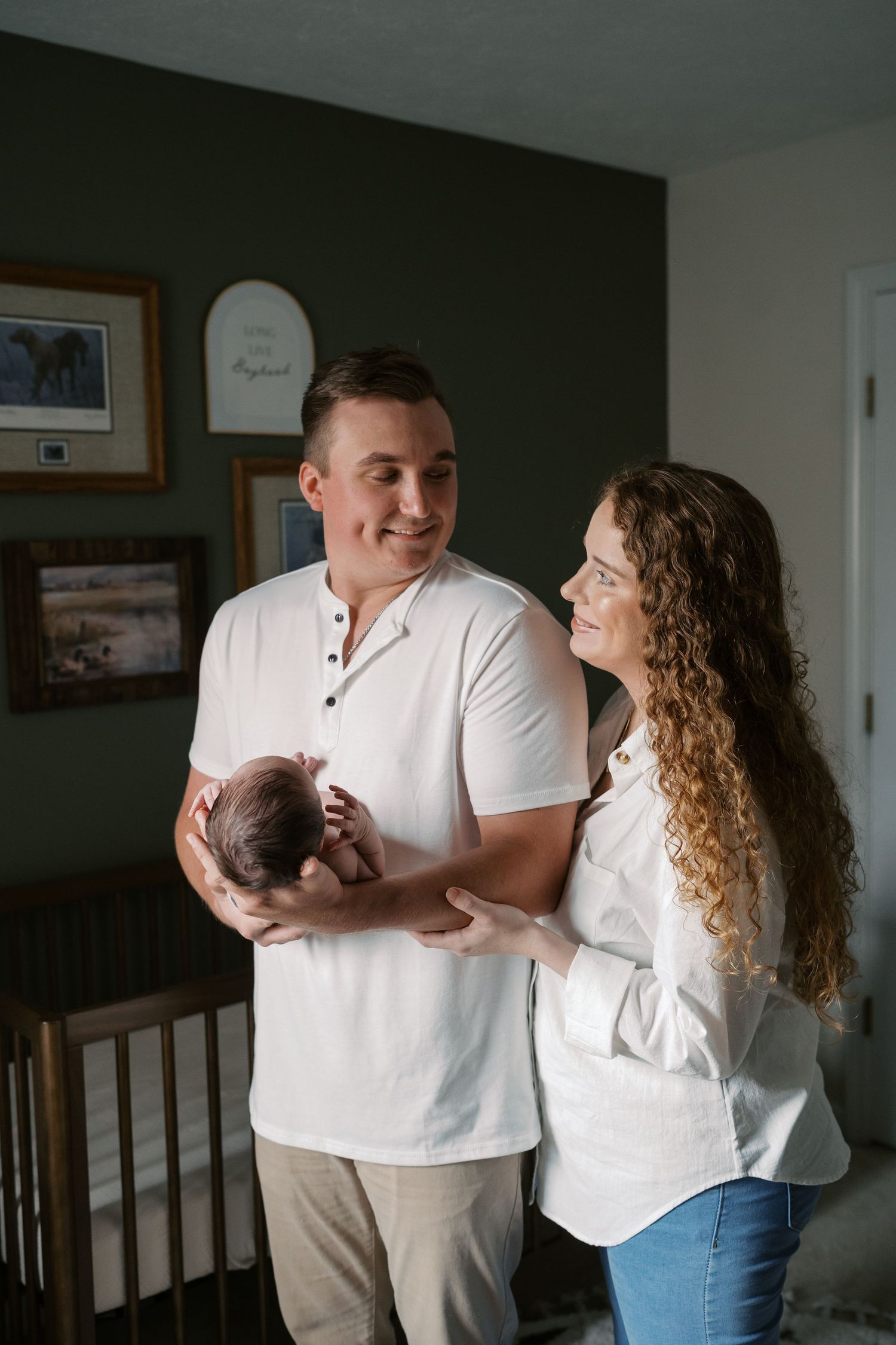 Couple in white shirts sharing tender moments with their newborn baby in a nursery setting.
