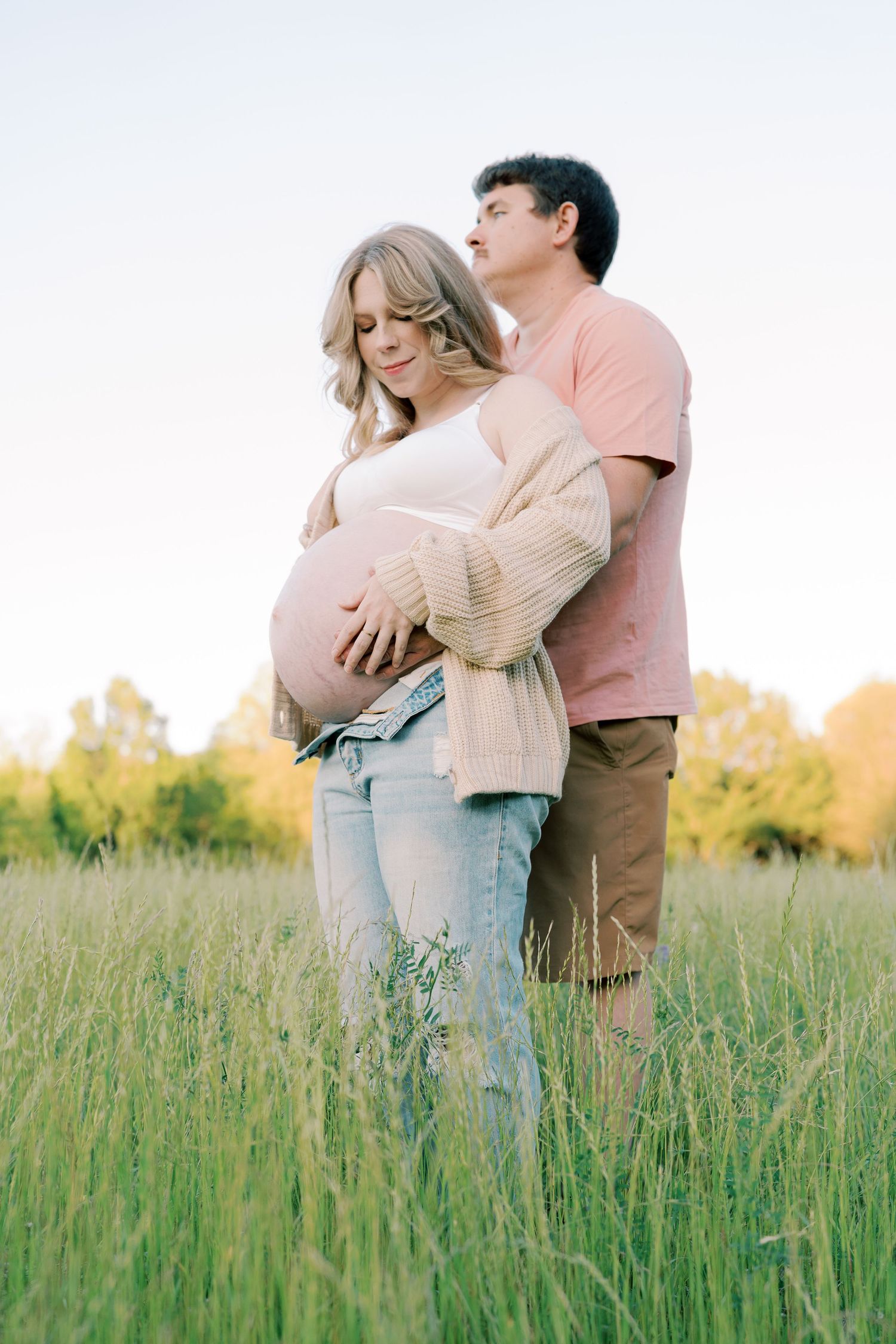 A couple embraces tenderly in a field of tall grass during a golden sunset.