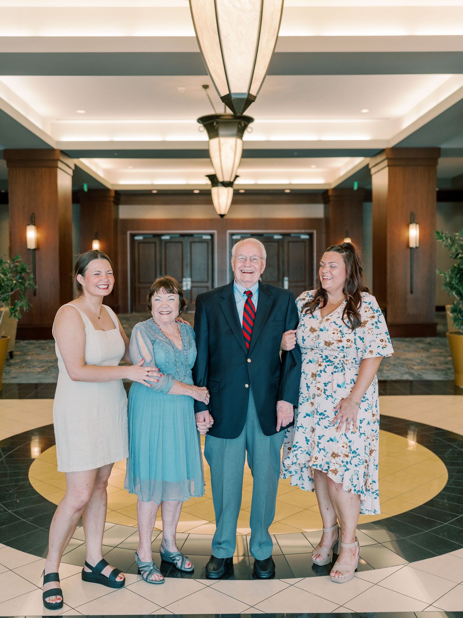 Multi-generational family group posing together in an elegant hotel lobby with tiled floors and pendant lighting.