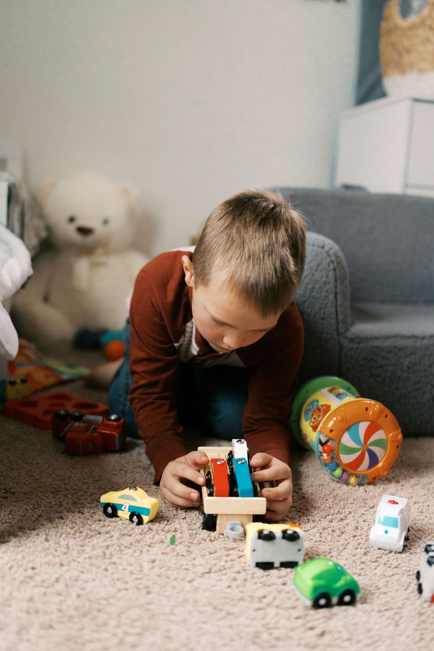 Child playing with wooden toy cars and blocks on beige carpet.