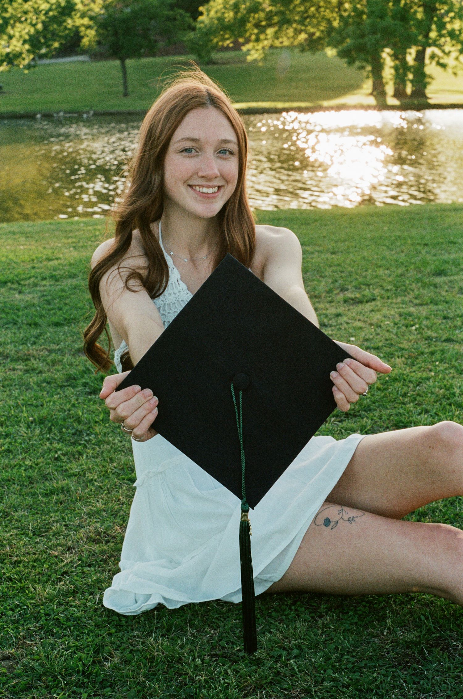 Casual graduation photoshoot on grass with white dress and black cap and gown.