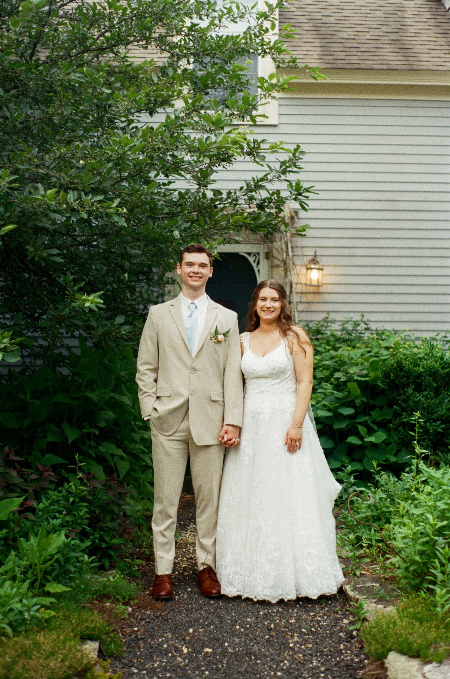 A wedding portrait in front of a white building surrounded by lush garden landscaping.
