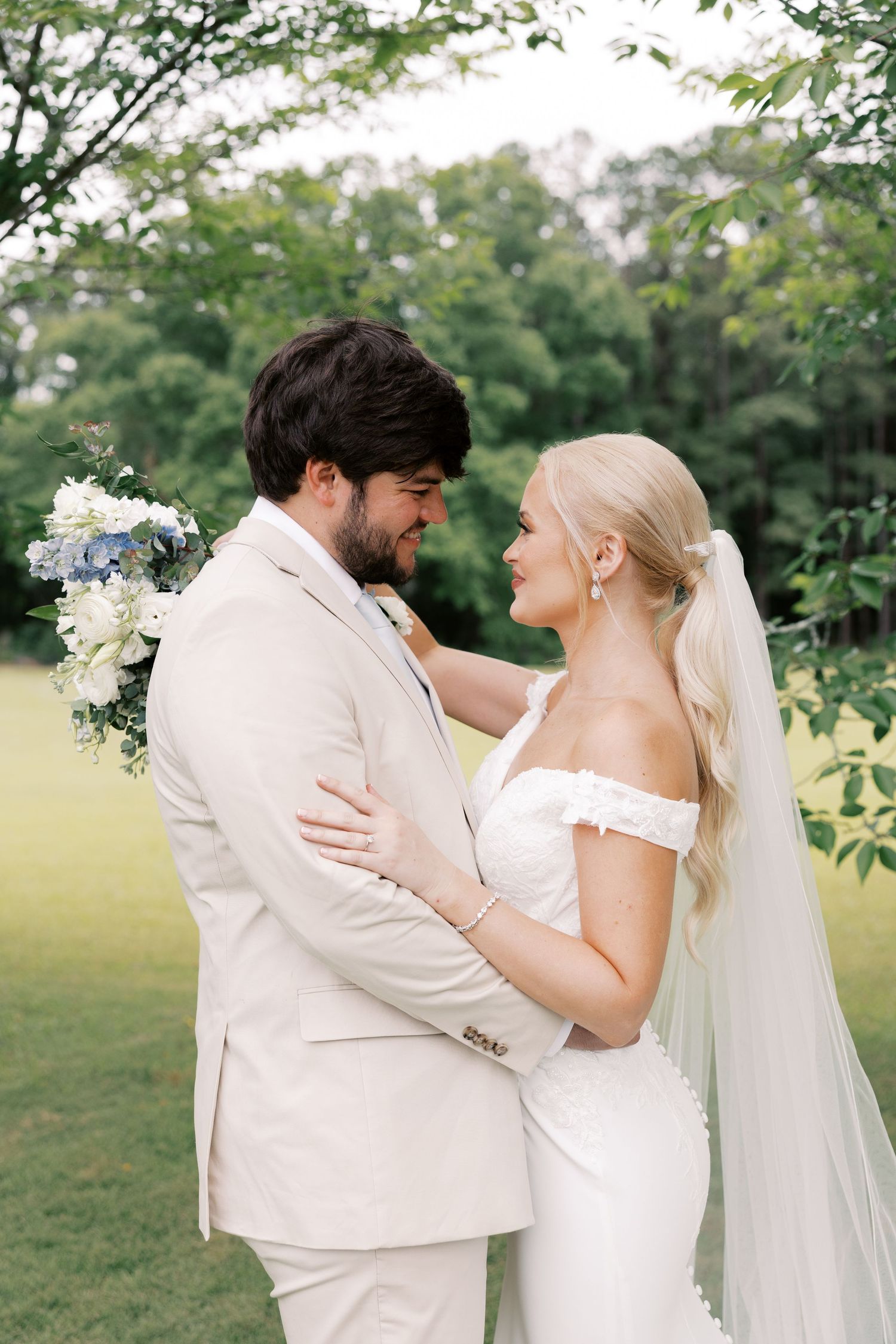 Wedding couple embracing outdoors during romantic photoshoot with cream and white attire.