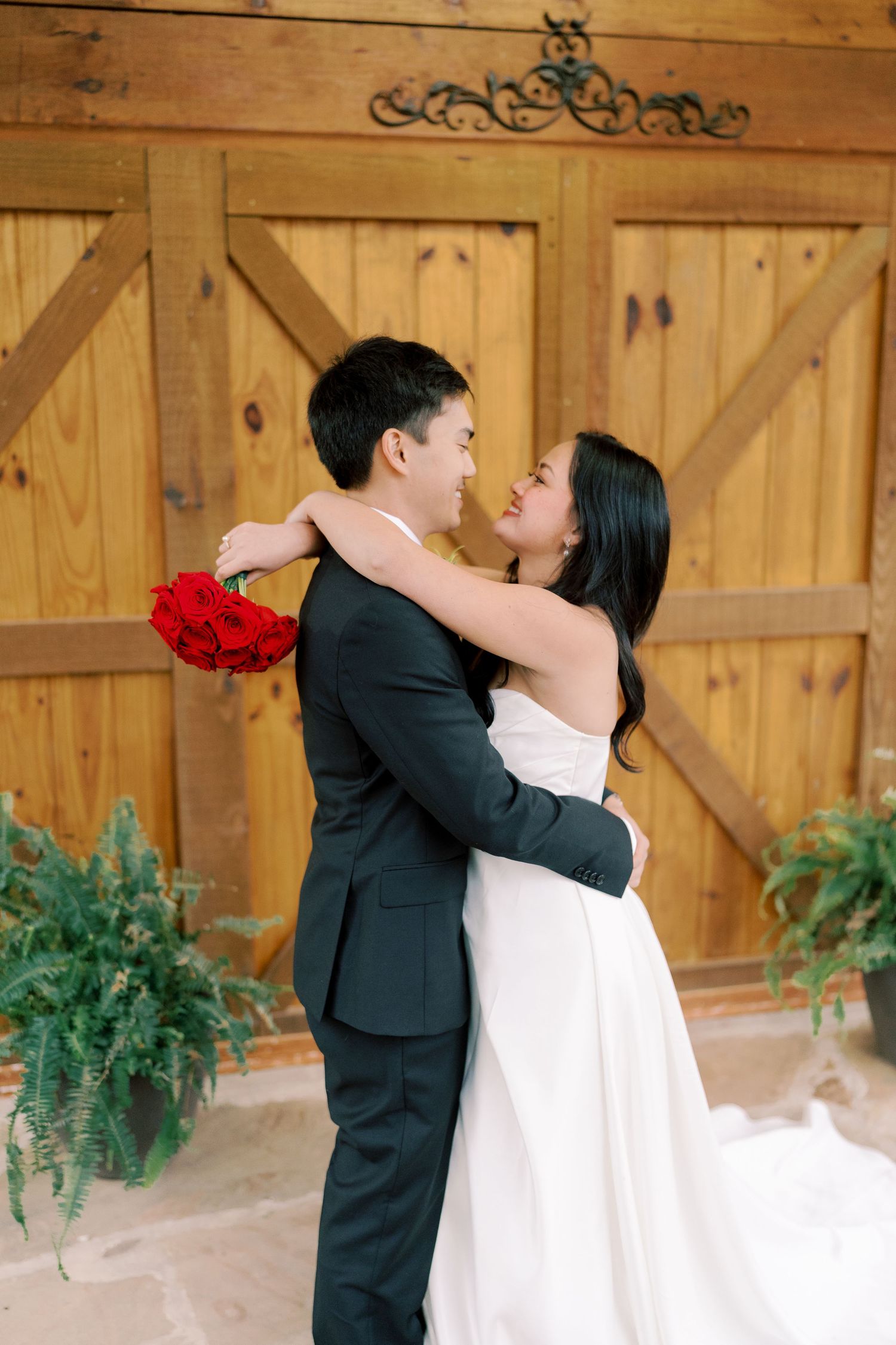 Couple shares romantic embraces against rustic wooden barn doors during wedding portraits.