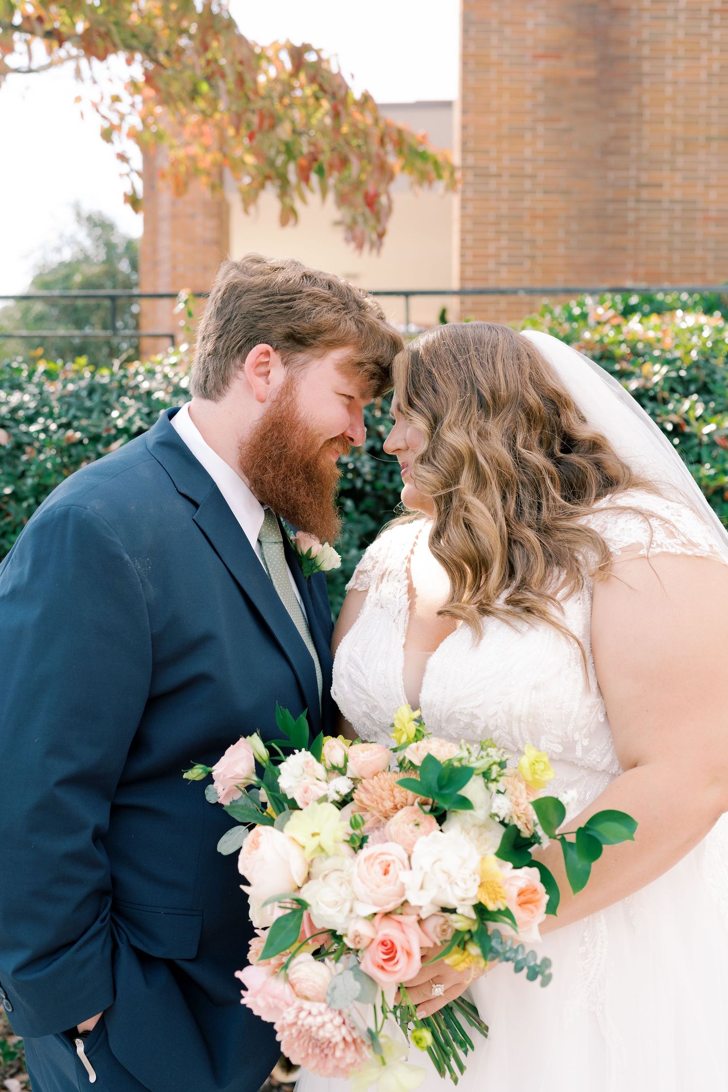 A tender moment between newlyweds with a beautiful peach and white bouquet.