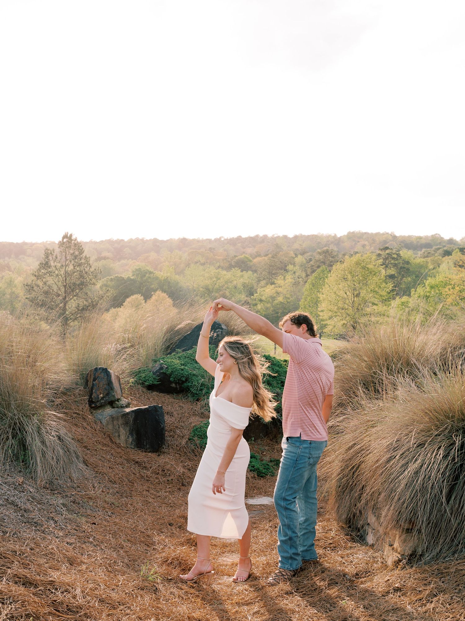 A couple dances together on a hillside during golden hour.
