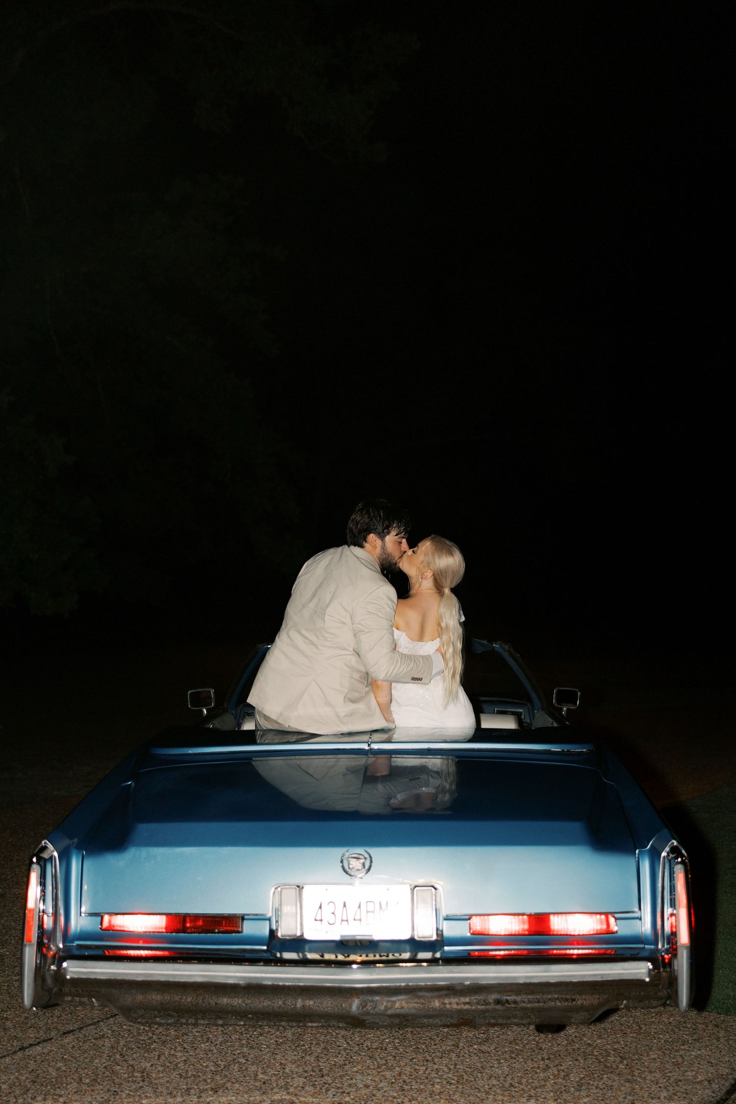 Back view of vintage blue Cadillac at night with brake lights glowing.