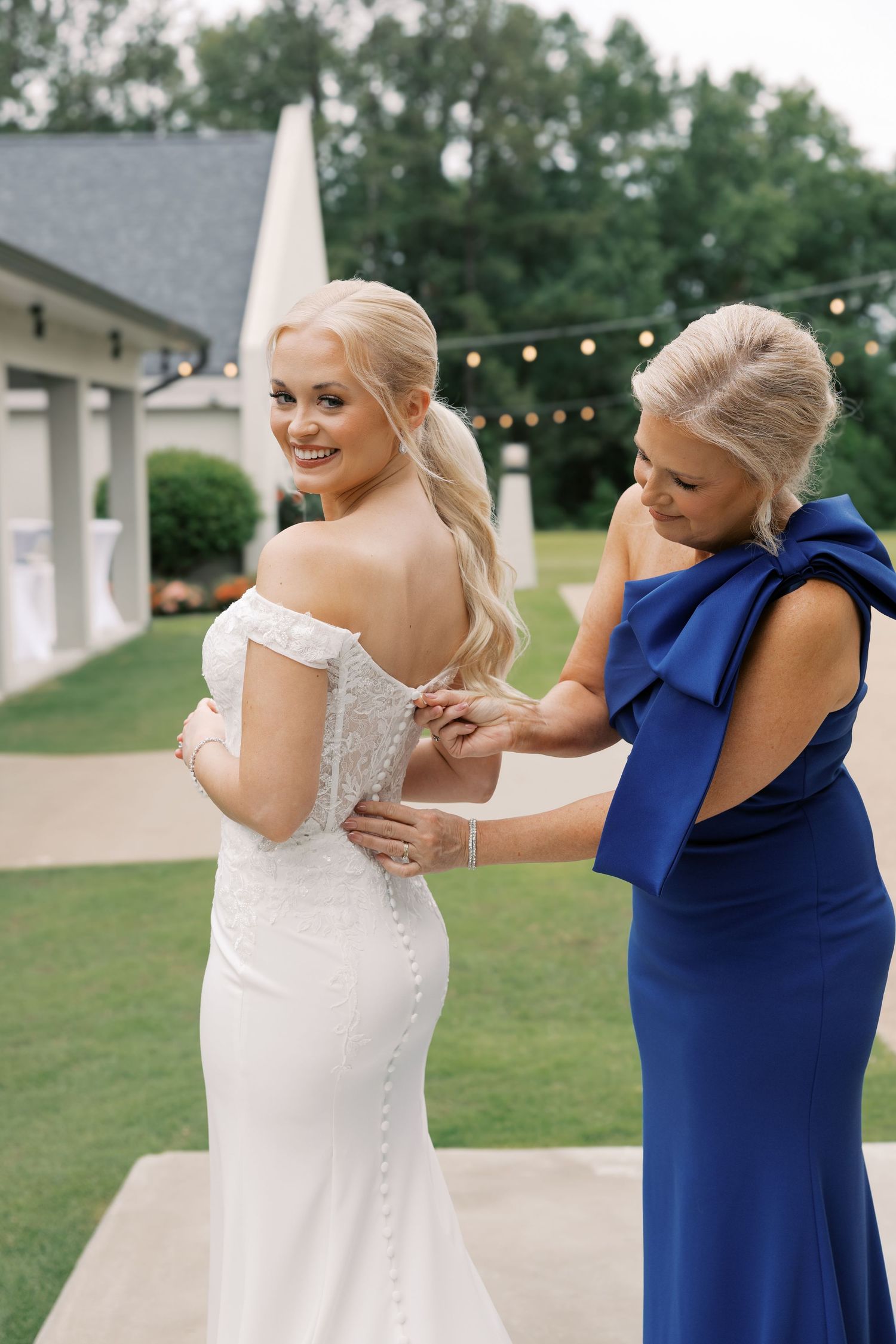 Wedding party in white dress and navy blue gown sharing a candid moment outdoors.