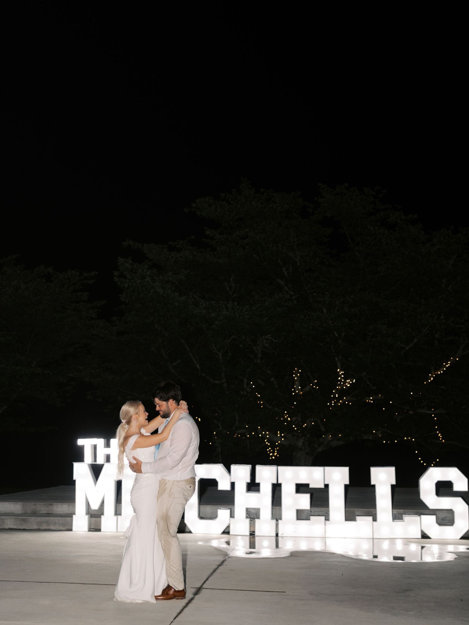 Large illuminated letters spelling out names create a romantic nighttime wedding backdrop.