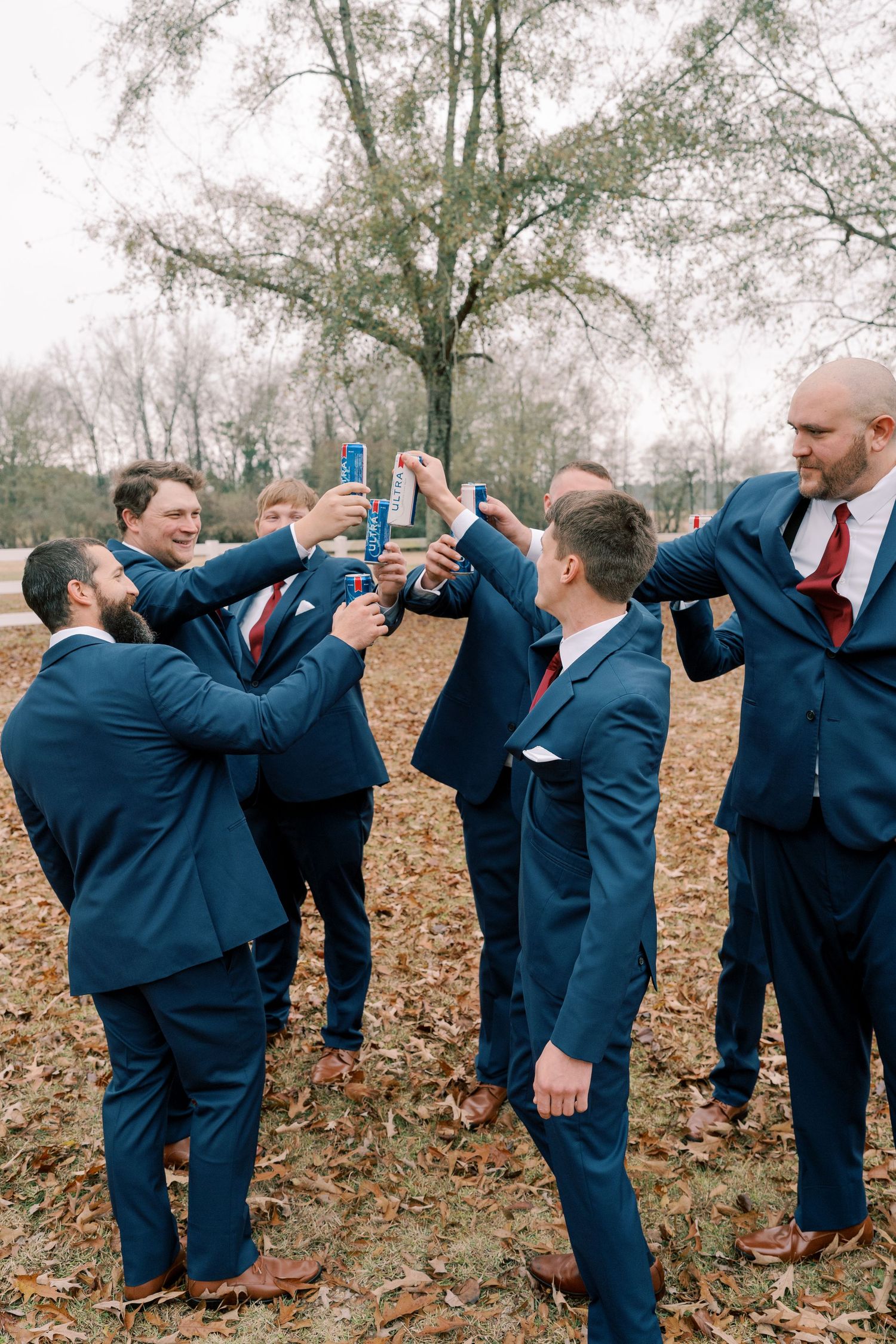 Groomsmen in navy suits toast and celebrate during outdoor wedding photoshoot.