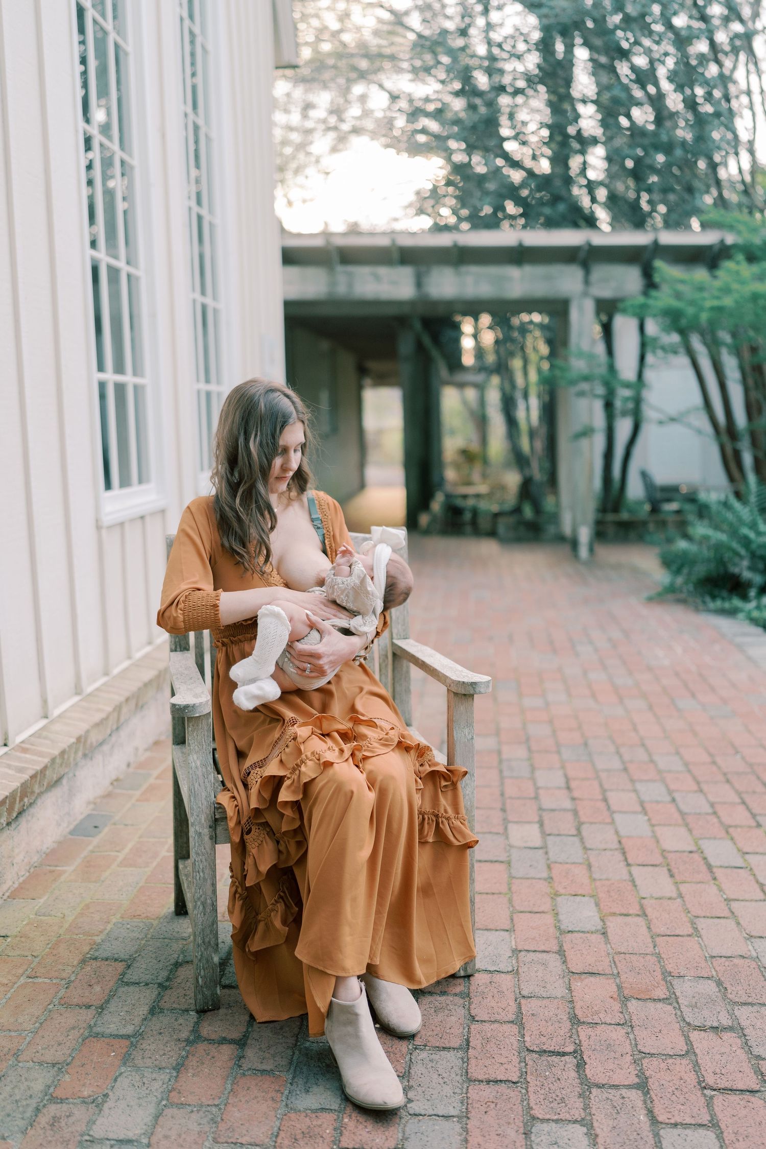 Woman in rust-colored dress sitting on brick patio near white building.