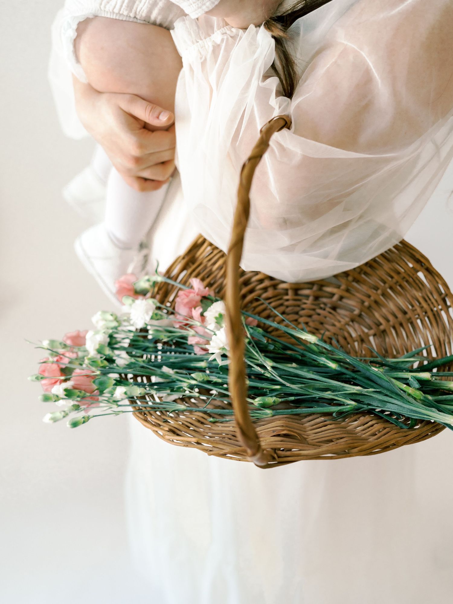 Hands arranging fresh flowers in a woven basket against white background.