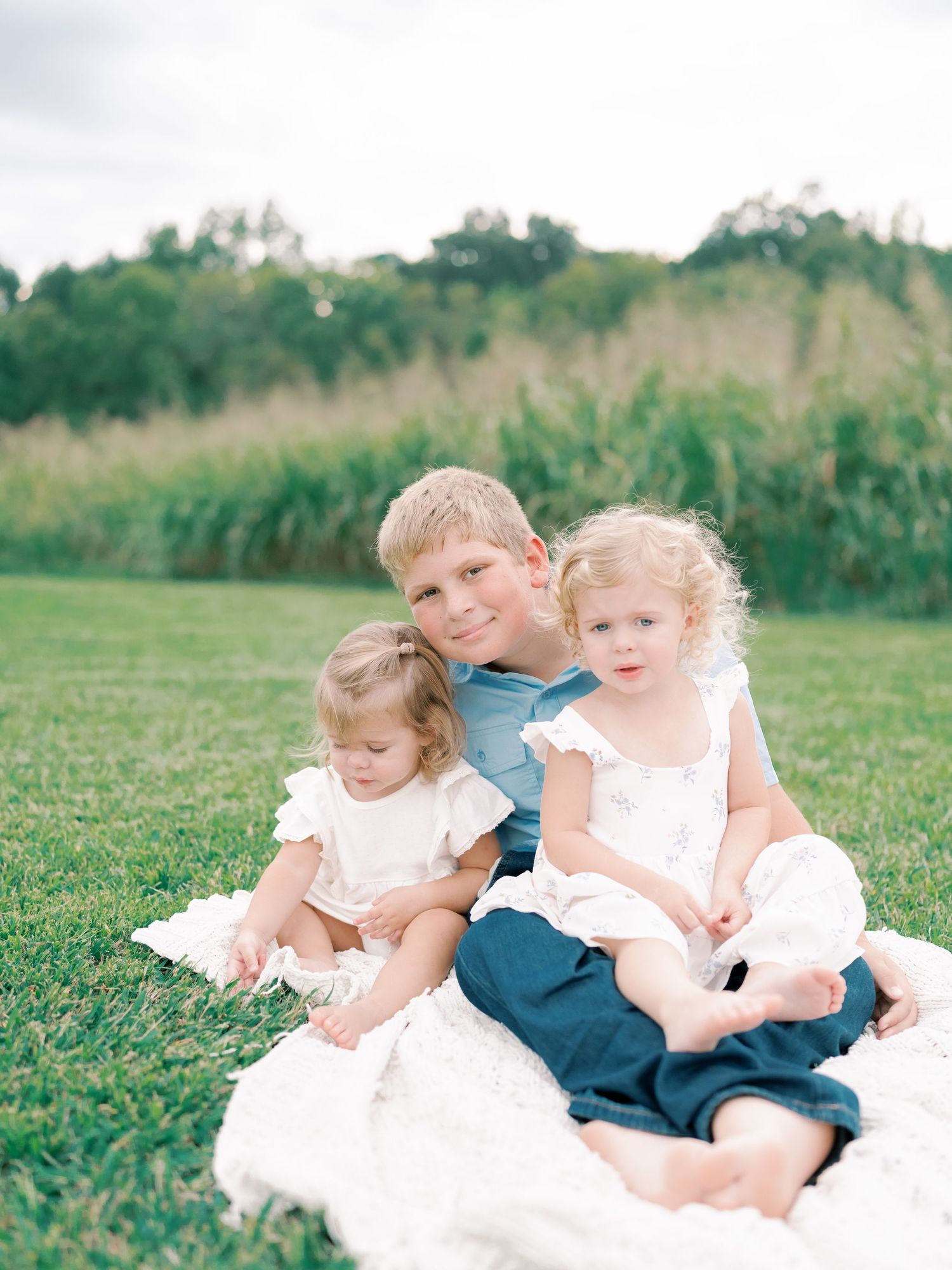 Children in white dresses and navy blue outfits play together on a grassy field during a photo session.