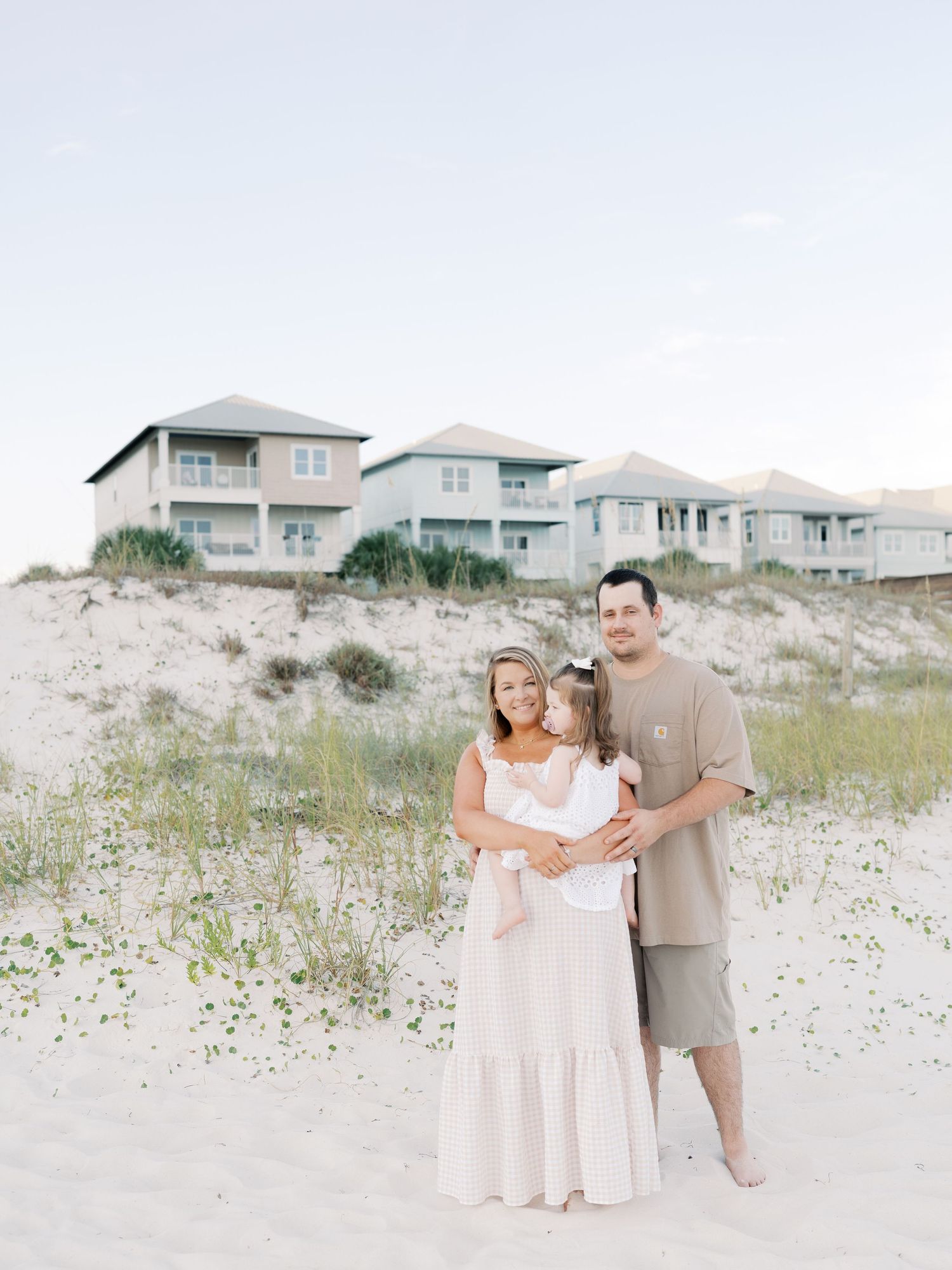 Candid family moment captured during beach photoshoot with coastal homes in background.