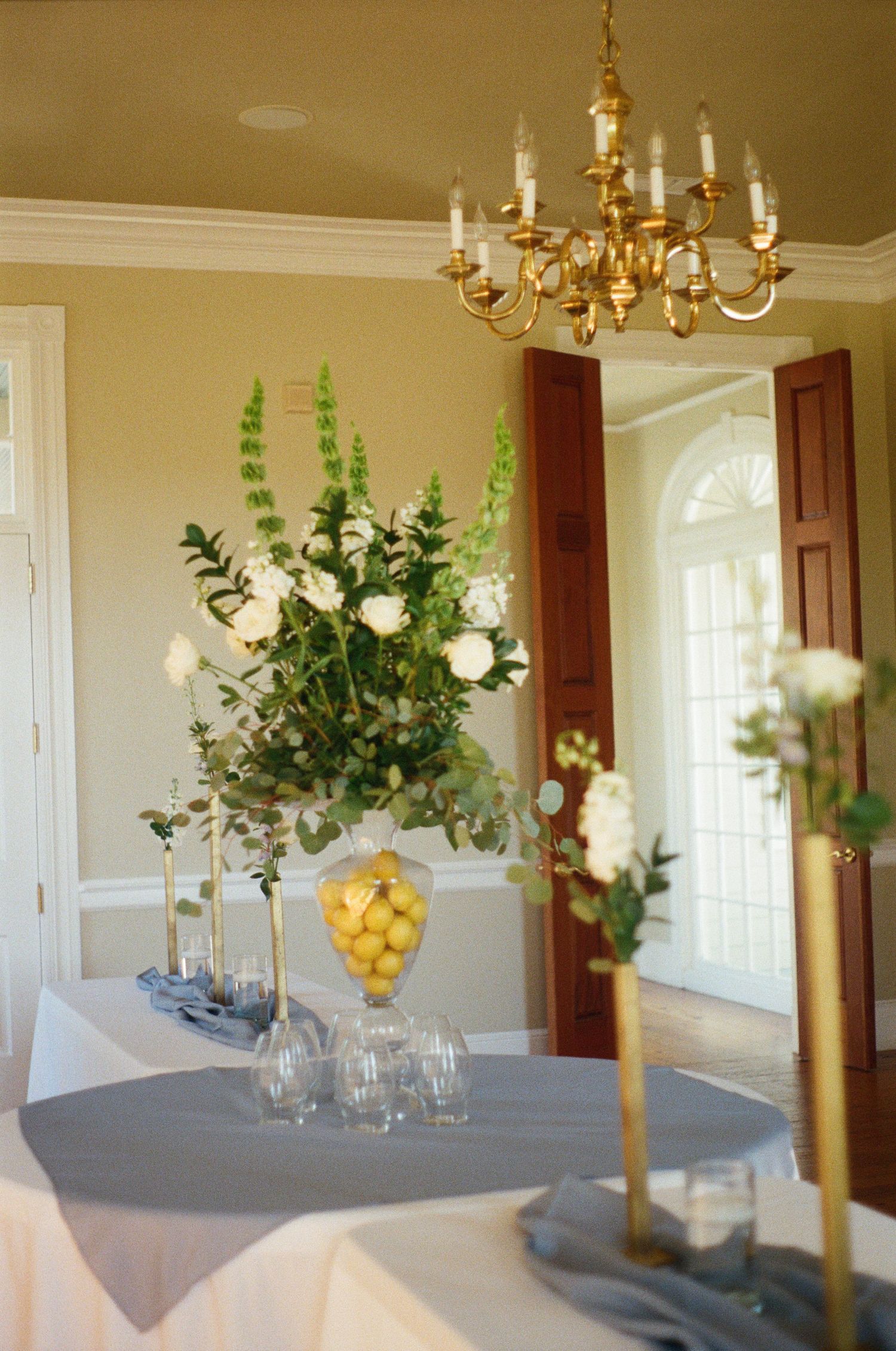 Elegant dining room with brass chandelier and floral centerpieces on tables.