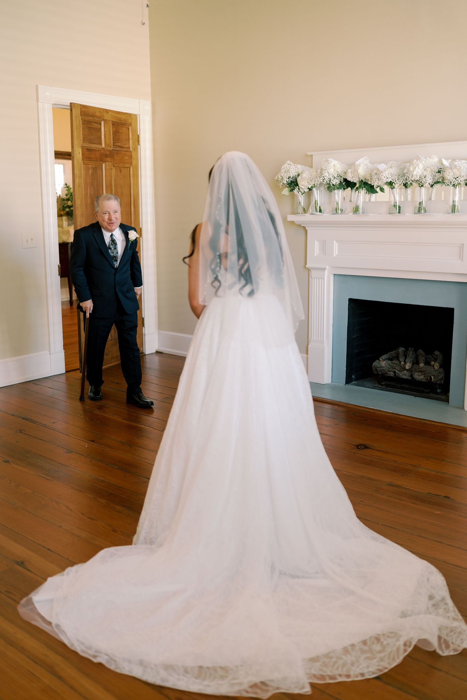 First look reveal with wedding dress and formal attire in an elegant room with fireplace.