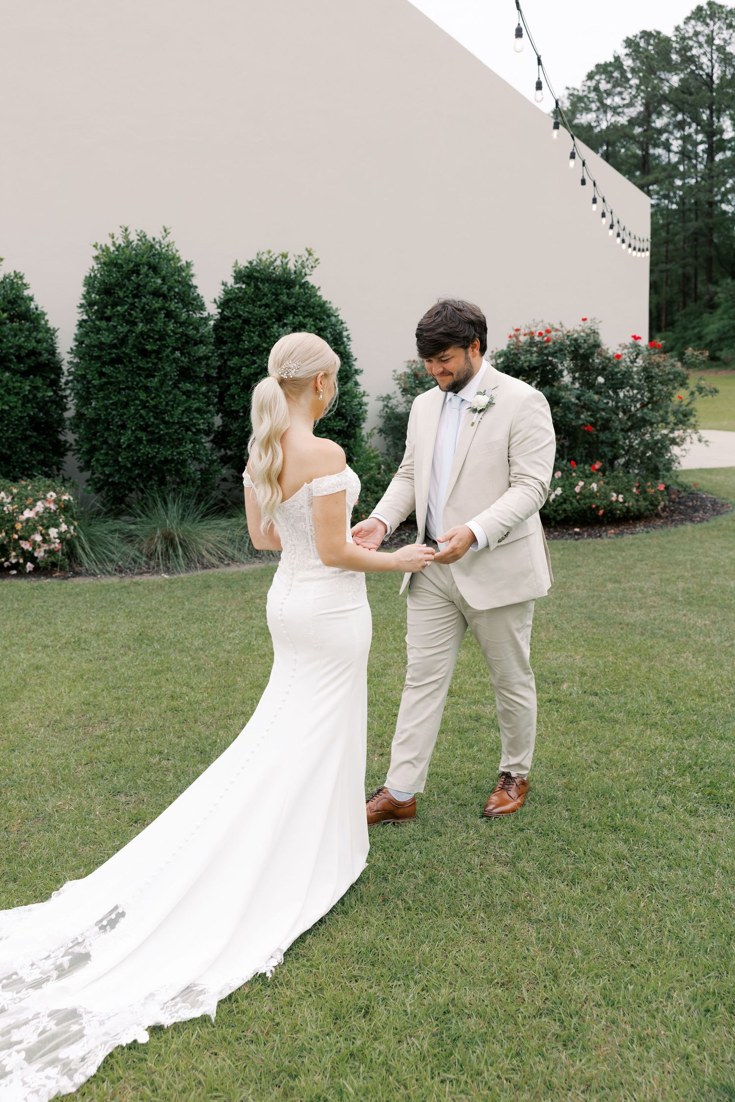 A couple shares their first look moment outdoors, with the bride's white dress train flowing on the grass.