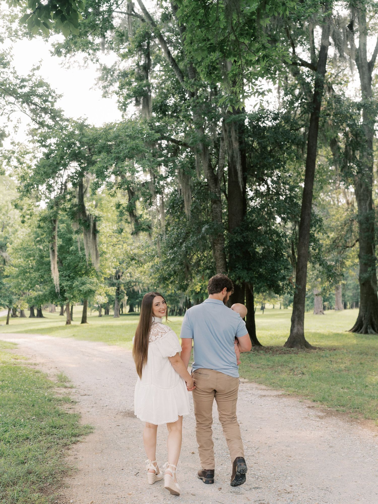 Three people take a casual stroll together on a winding dirt path through a park.