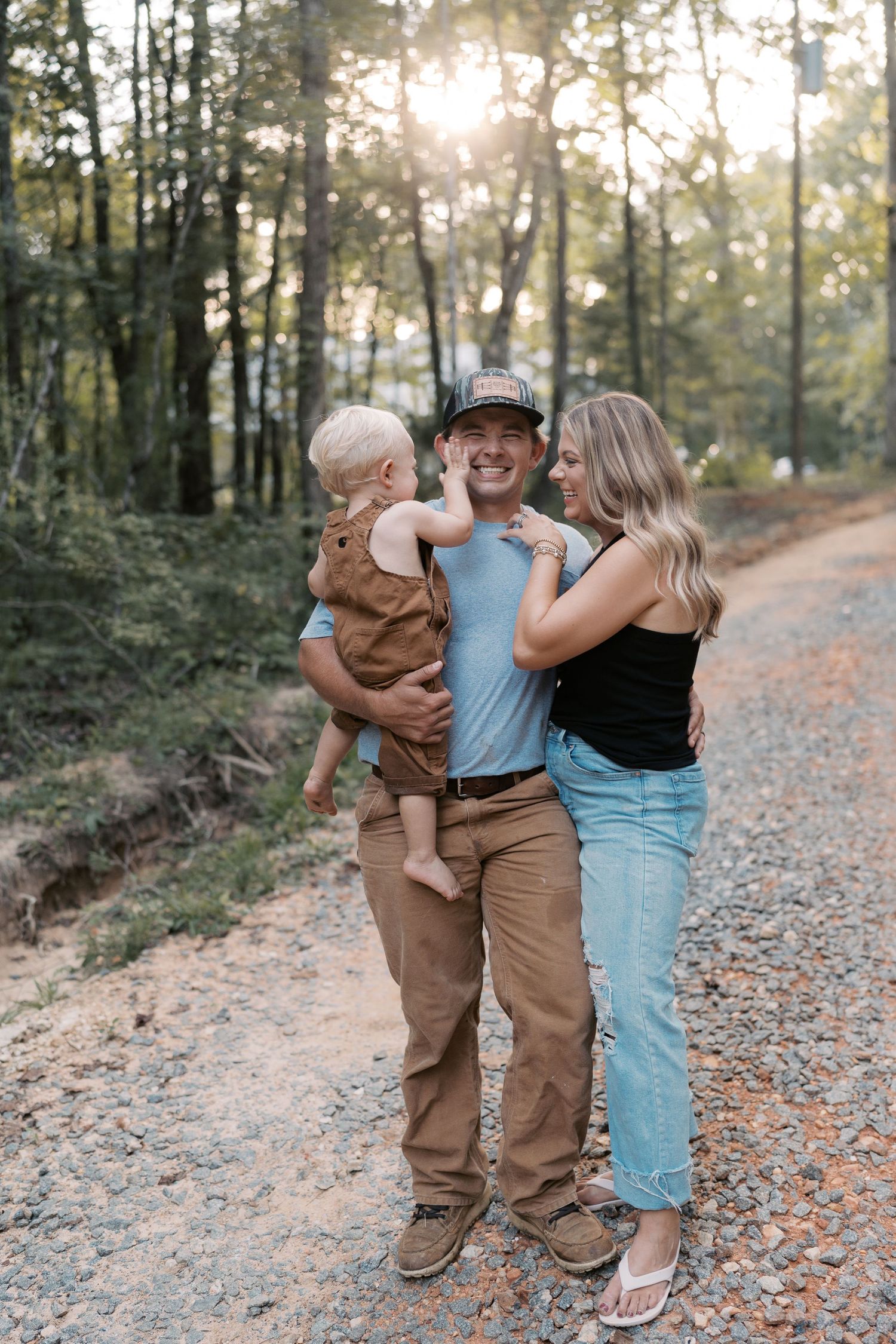 A happy family embraces while standing on a leaf-covered forest trail at sunset.