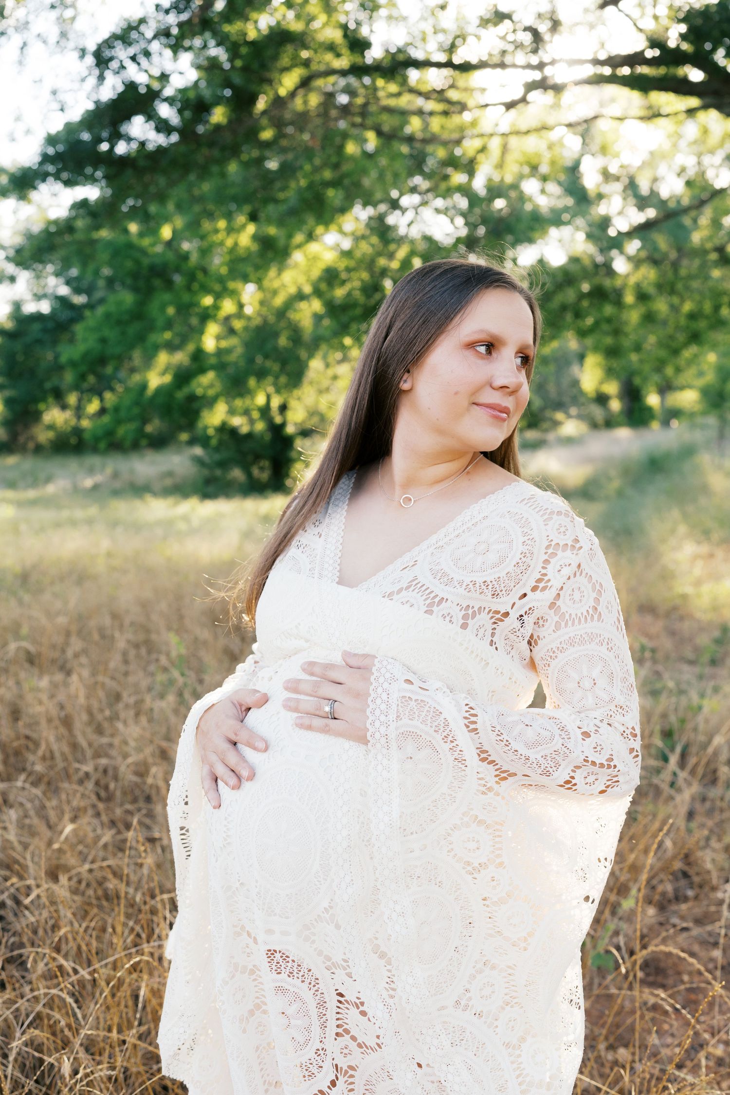 Romantic white lace maternity dress photographed in golden afternoon light.