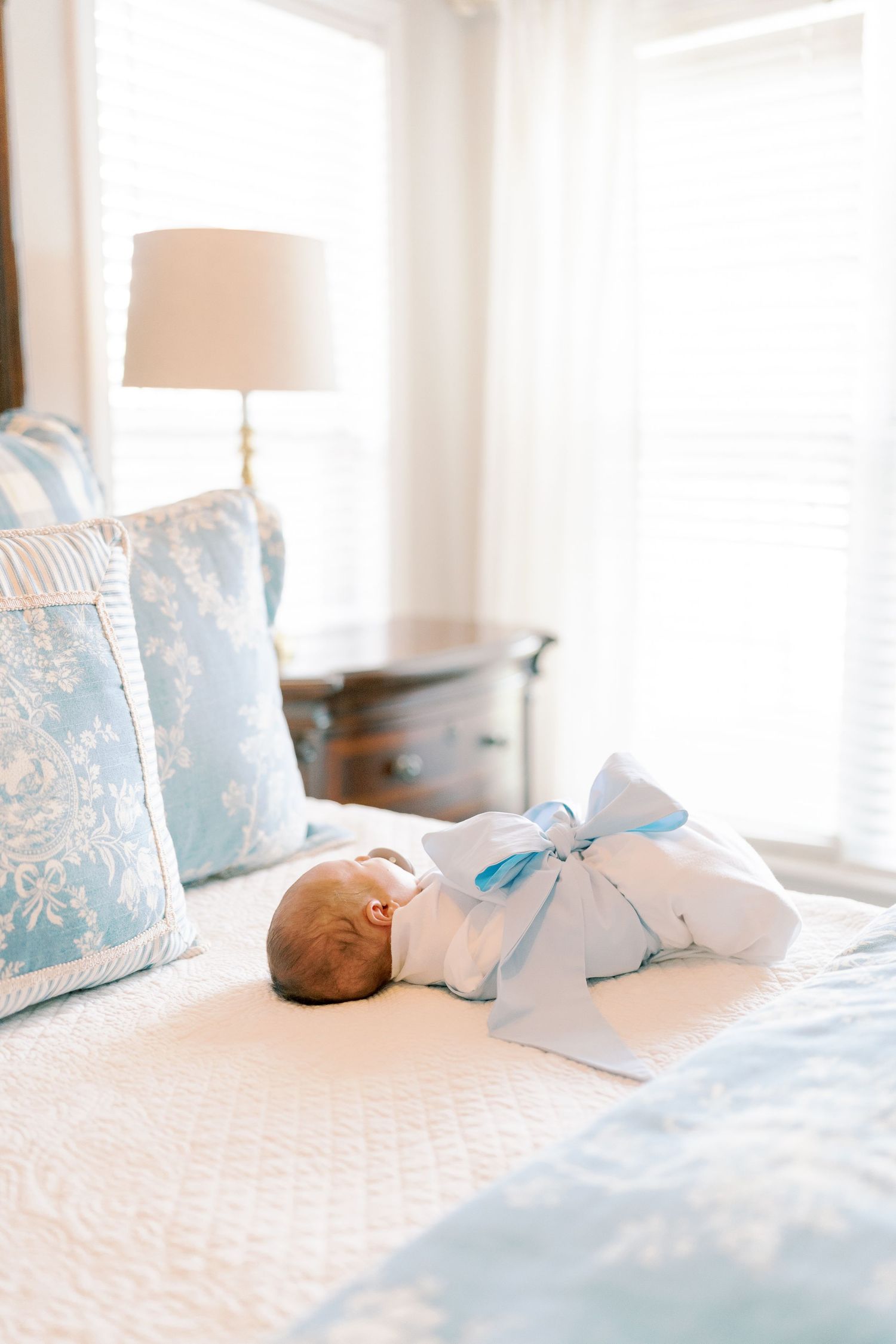 Newborn baby wrapped in blue bow sleeps peacefully on white bedding.