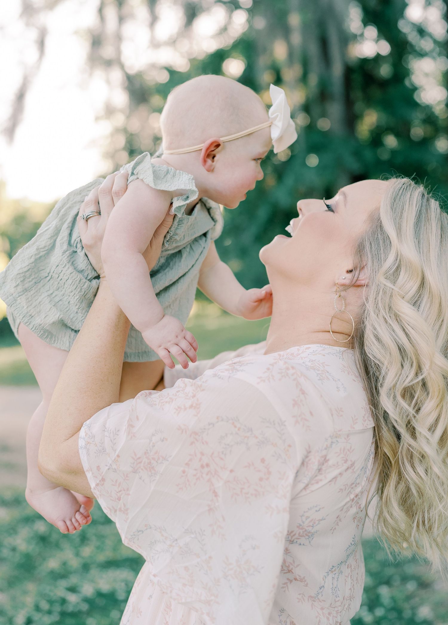 Joyful moments between parent and baby captured in soft, dreamy lighting outdoors.