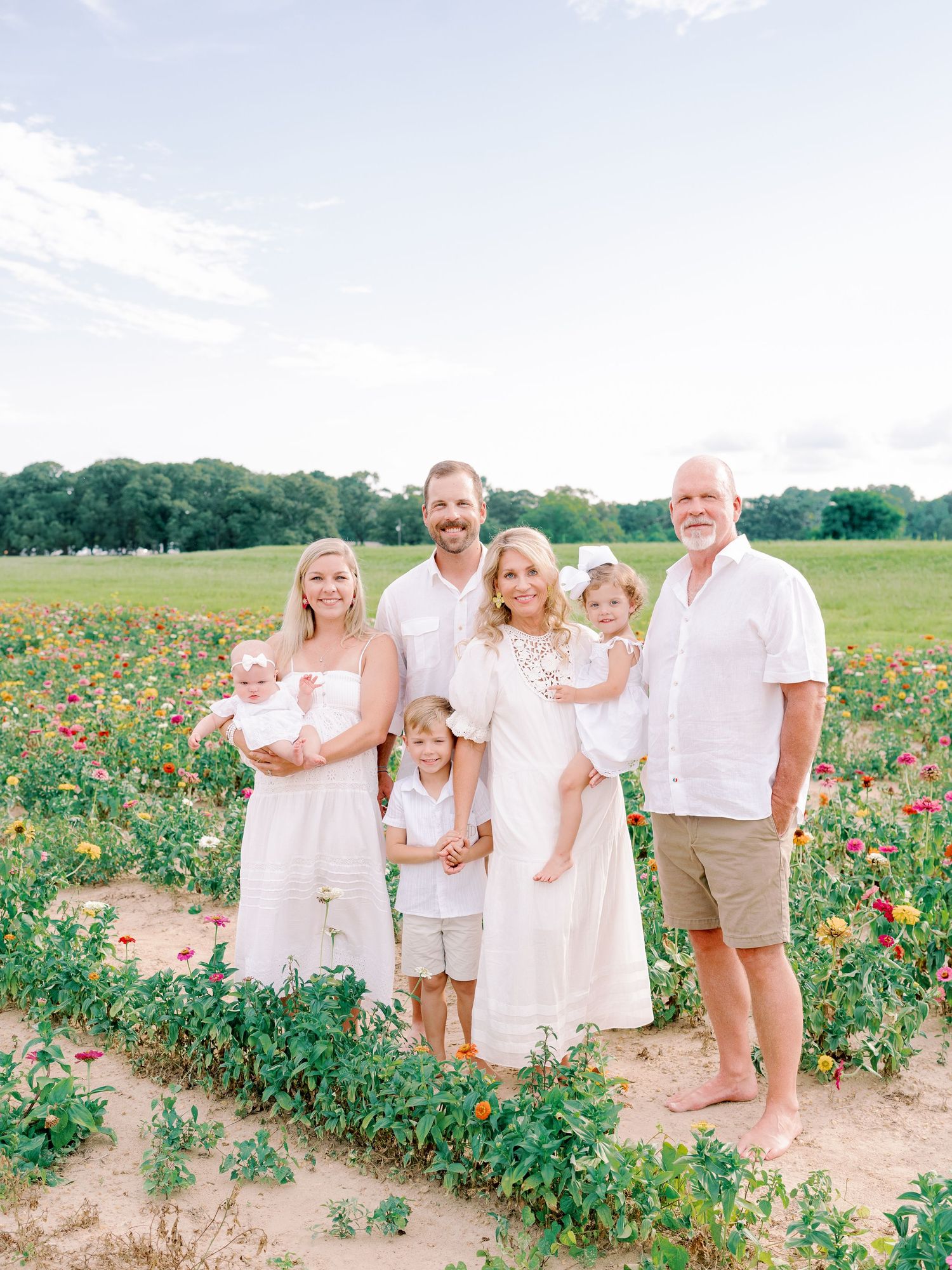 Family wearing white outfits poses together in a colorful flower field on a sunny day.