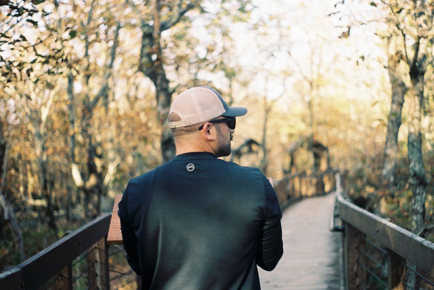 People walking along a wooden boardwalk path through autumn trees.