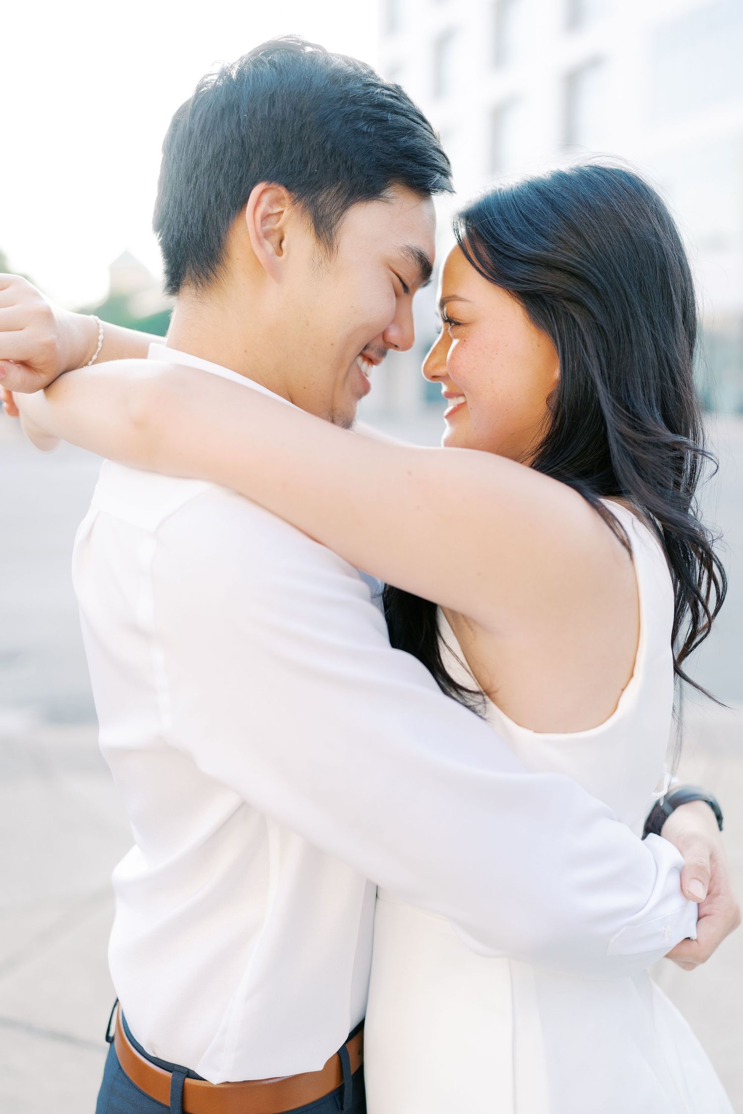 A couple embraces in white outfits during a bright outdoor photoshoot.