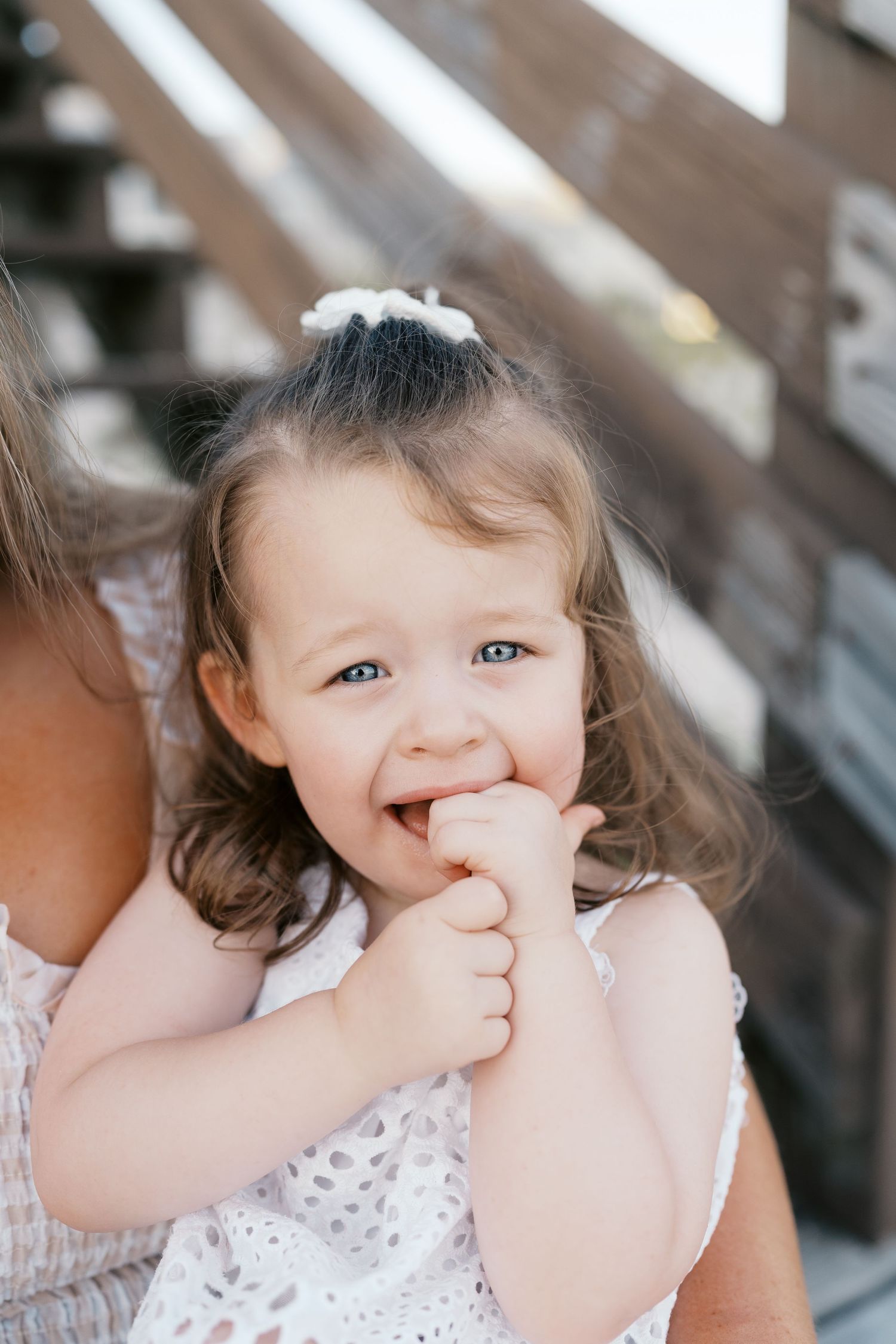 A small child in a white dress makes playful expressions while sitting on stairs.