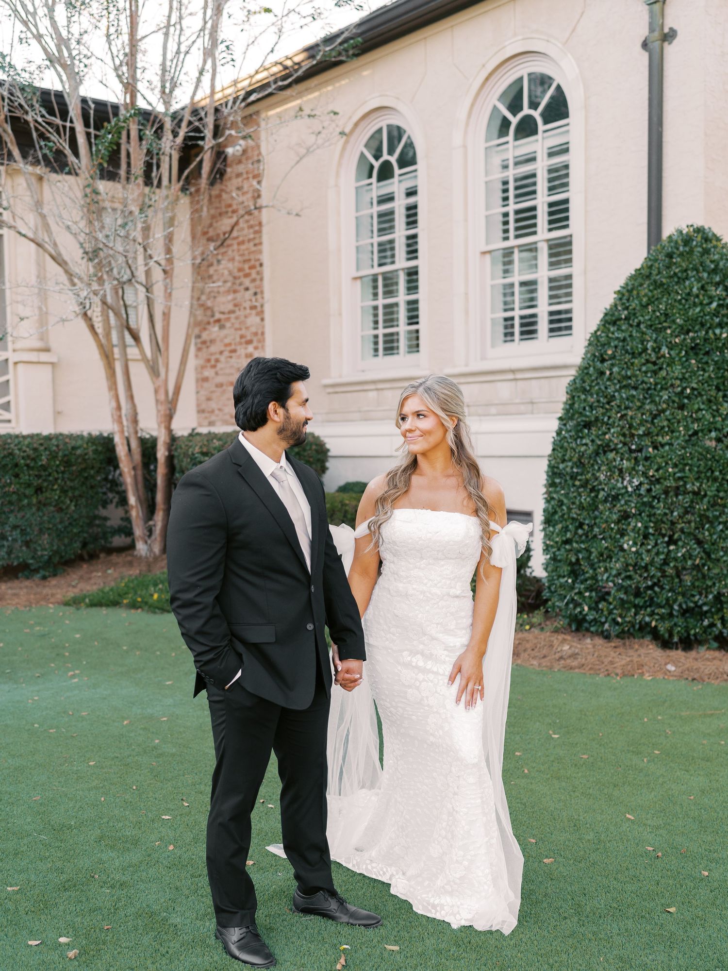 Elegant wedding couple poses in front of historic building with arched windows.