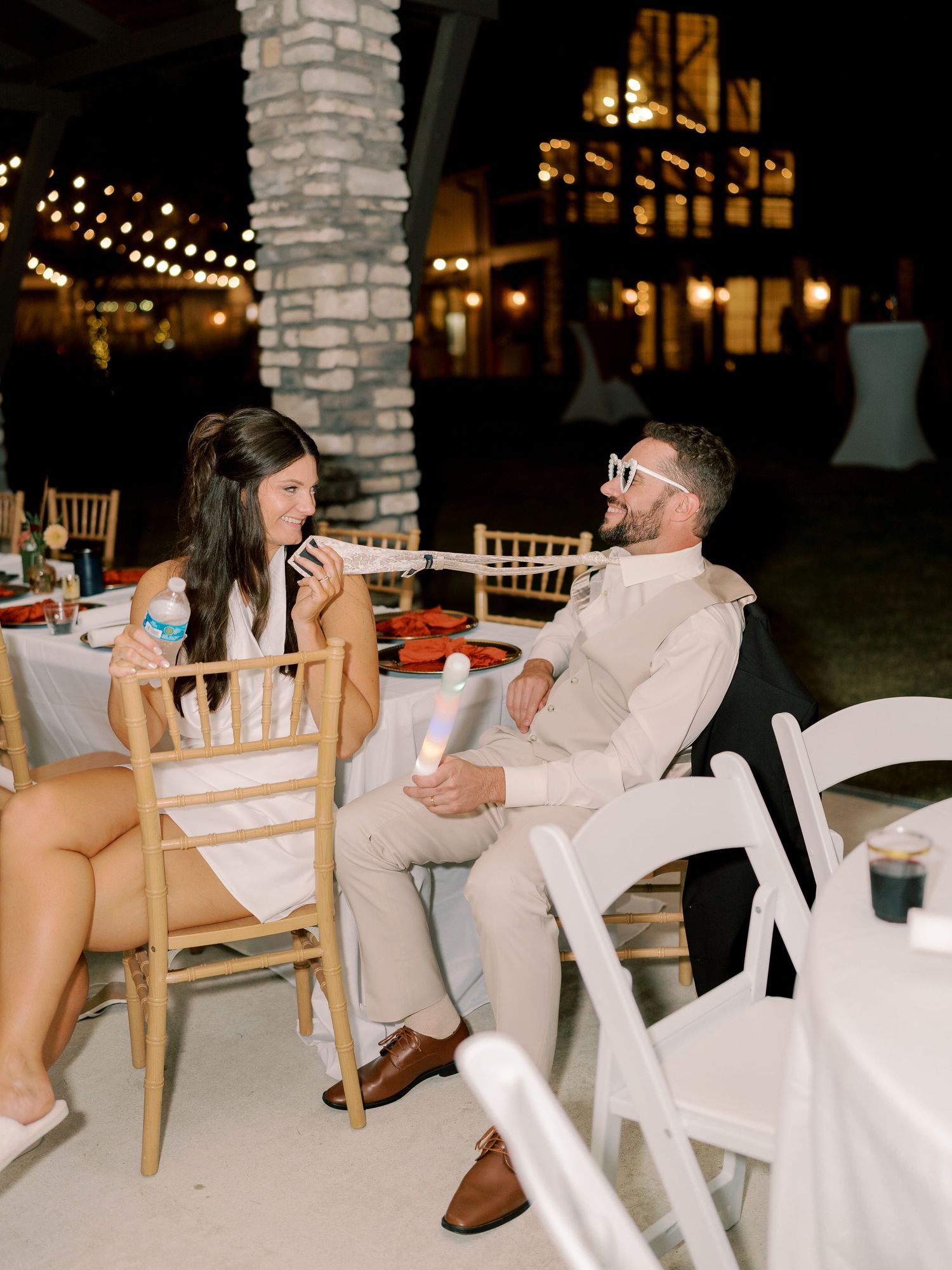 Wedding guests enjoying casual conversation at outdoor reception with string lights.