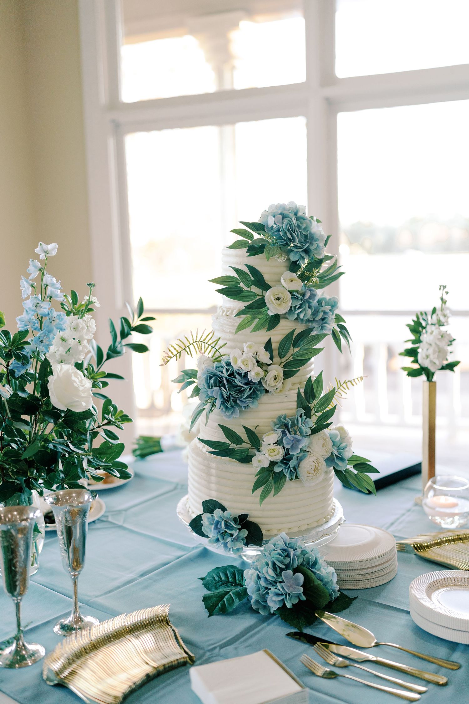 Elegant table setting with blue and white floral arrangements and gold accents for a wedding reception.