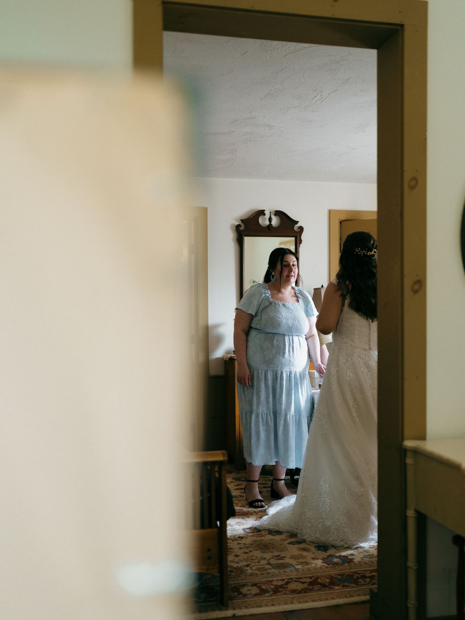 Wedding preparations captured through a doorway showing figures in light blue dresses.