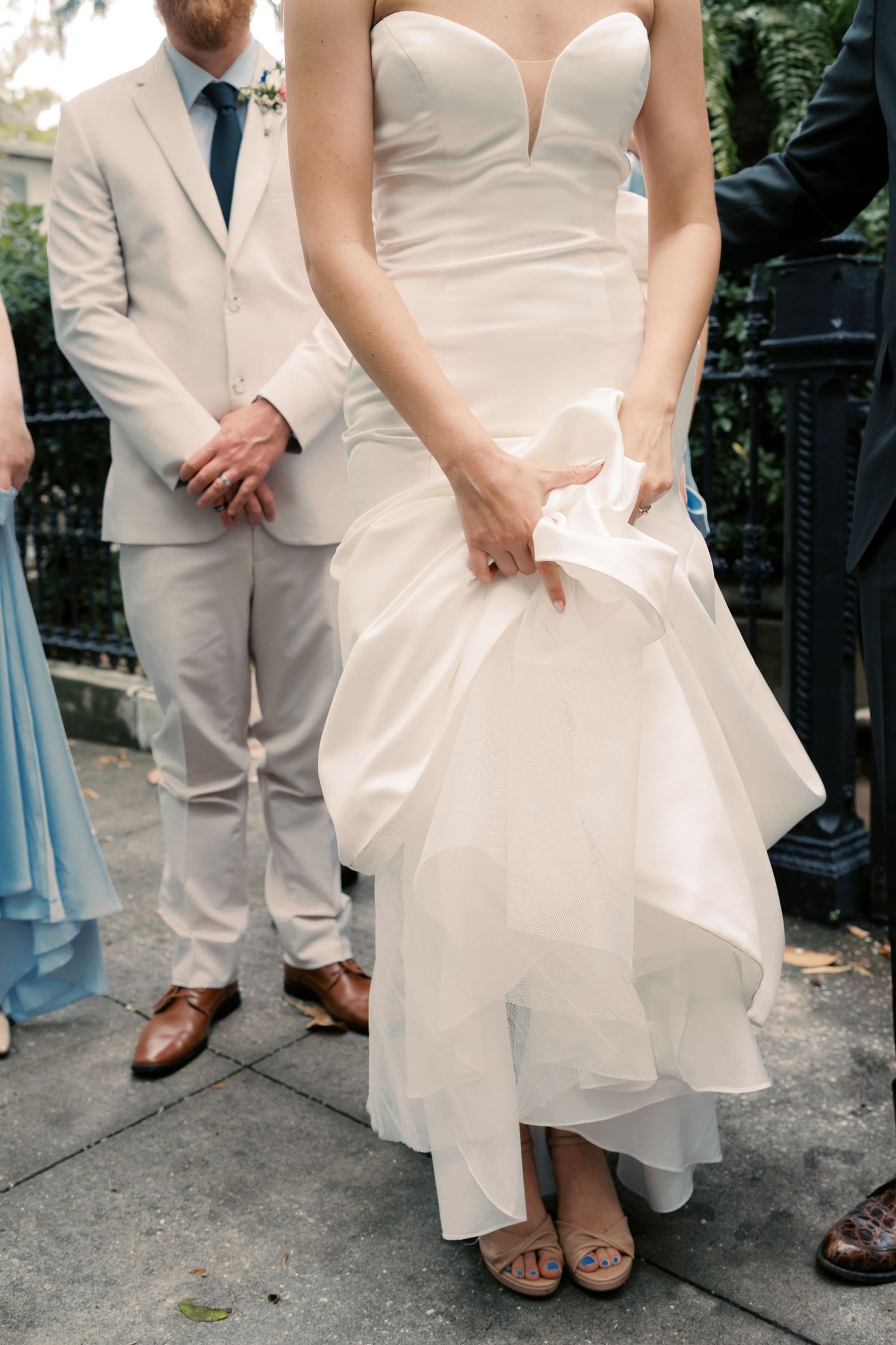 Wedding attire details showing white dress and beige suits at an outdoor ceremony.