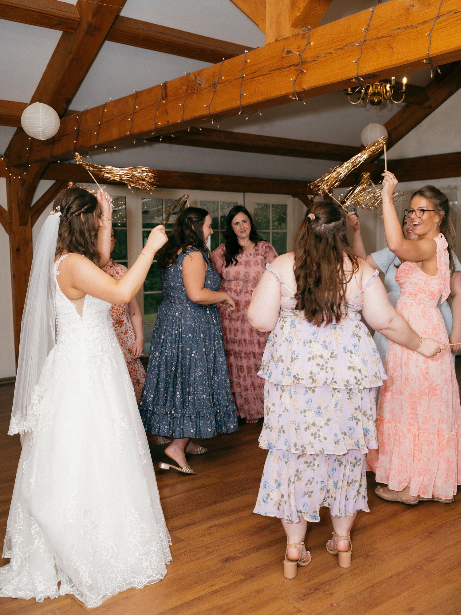Bridesmaids in floral and pastel dresses dance during a wedding reception.