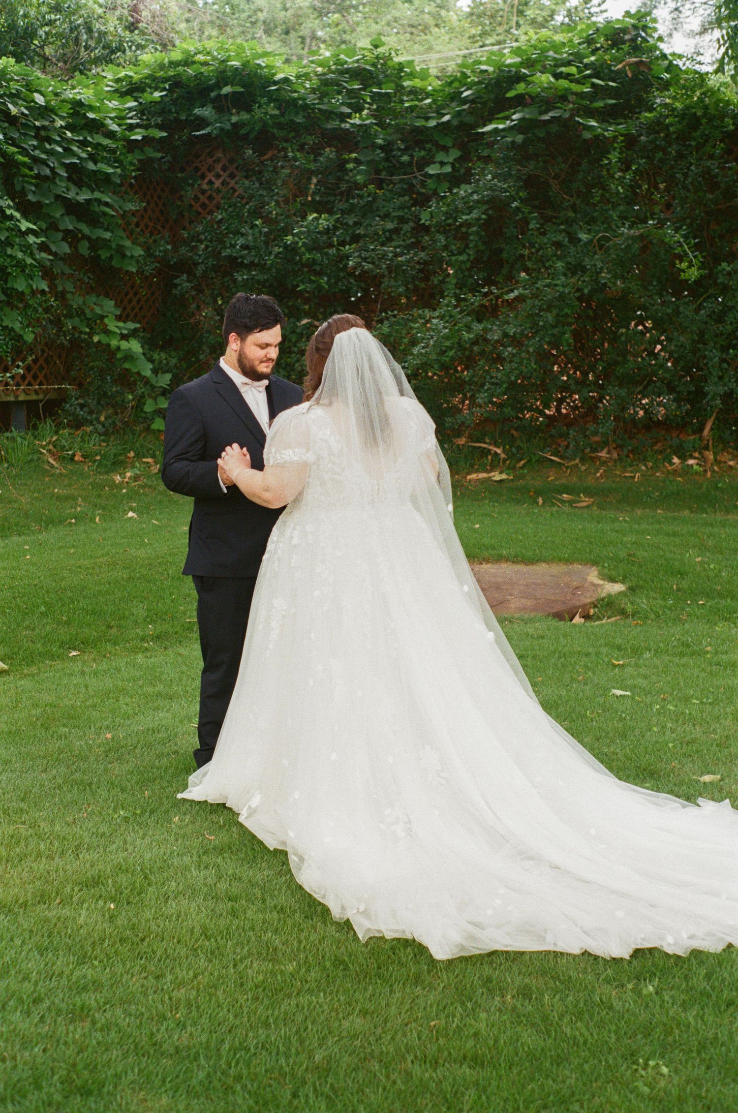 A flowing white wedding dress train trails across a lush green lawn during an outdoor photo session.