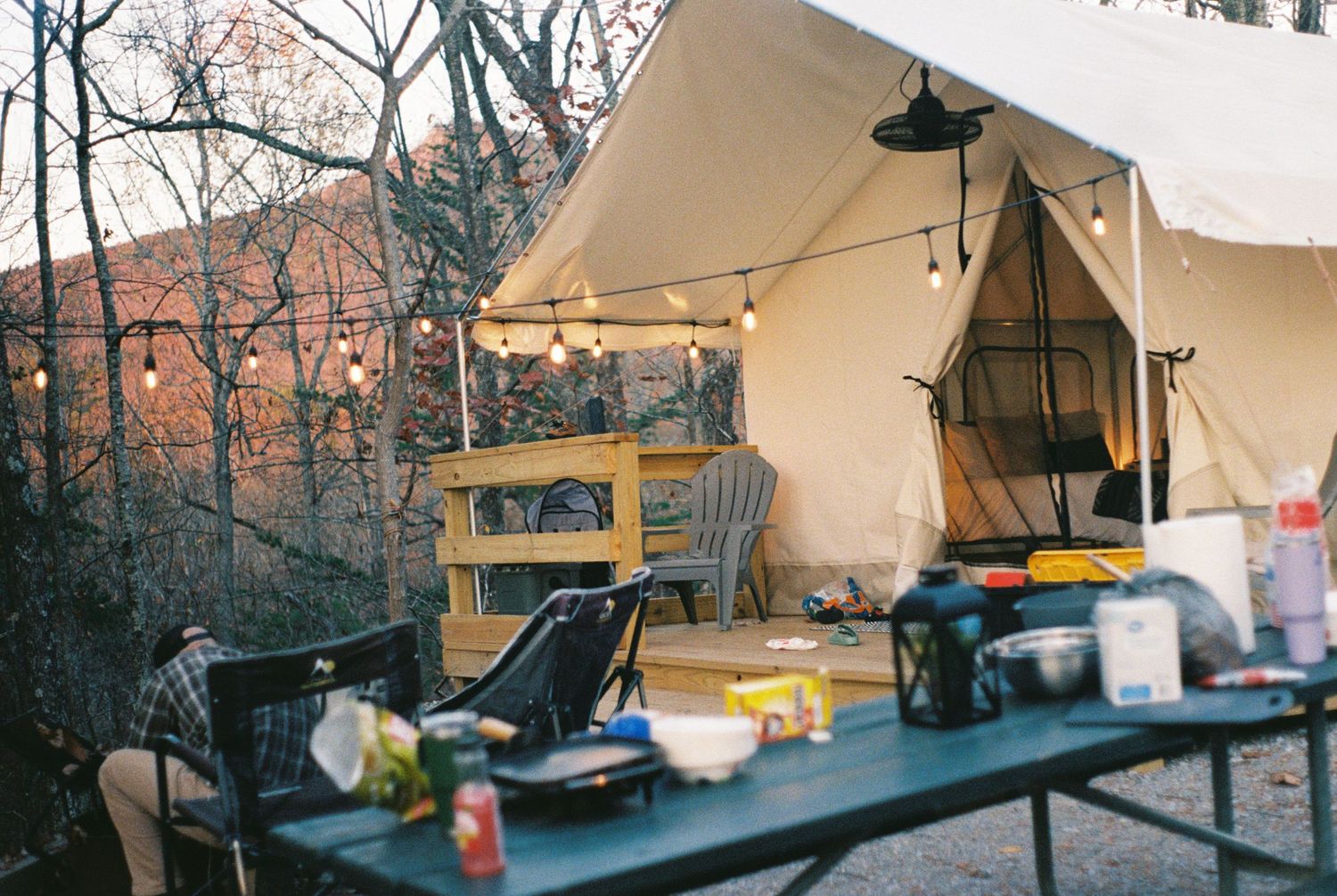 Outdoor camping setup with white canvas tent and string lights at dusk.
