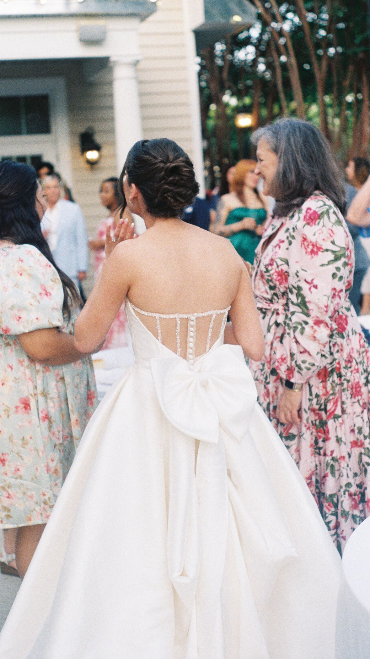 Row of bridesmaids in floral dresses showing intricate back details of their gowns.
