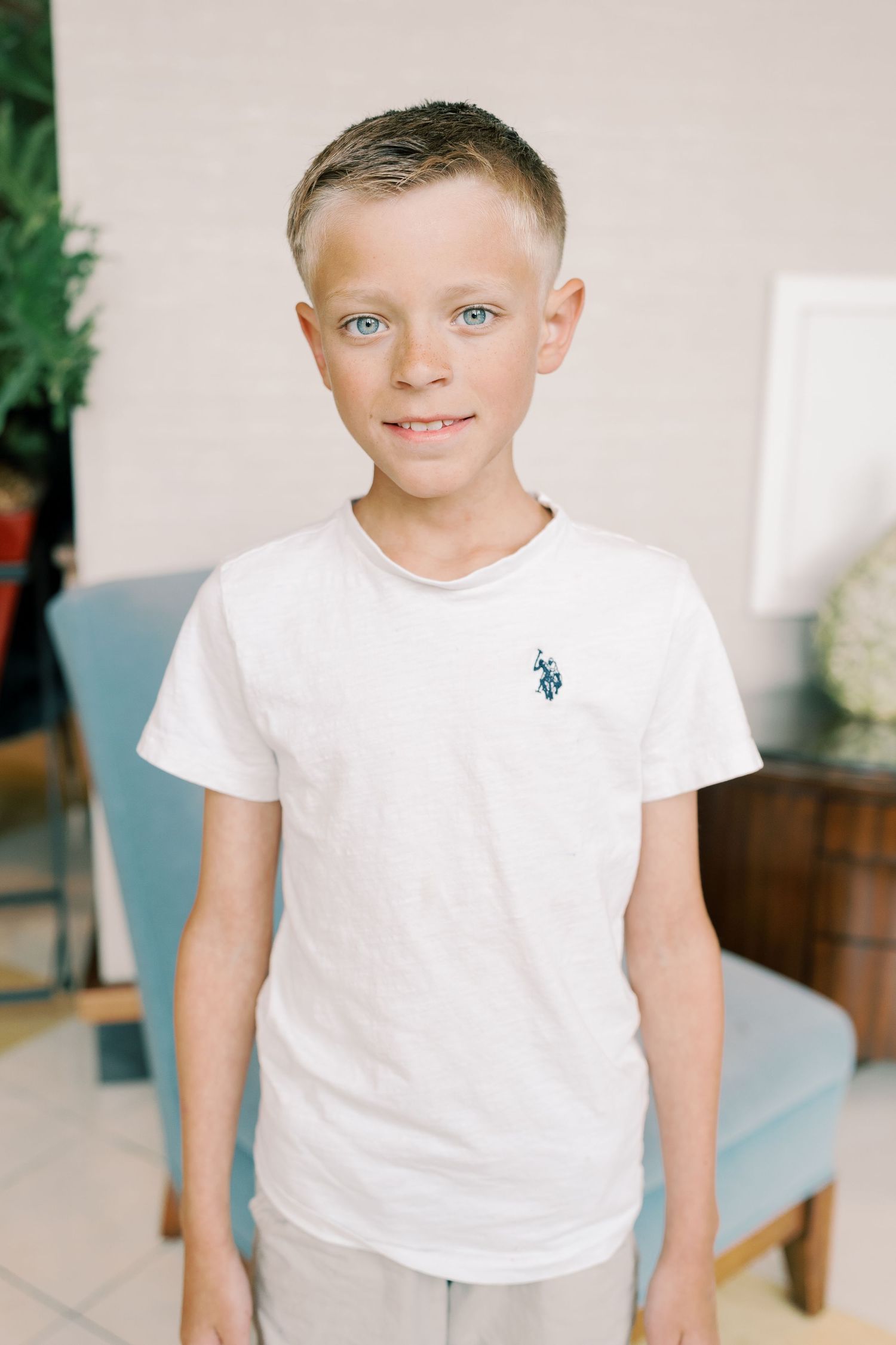 Child in white t-shirt with small logo posing against light background.