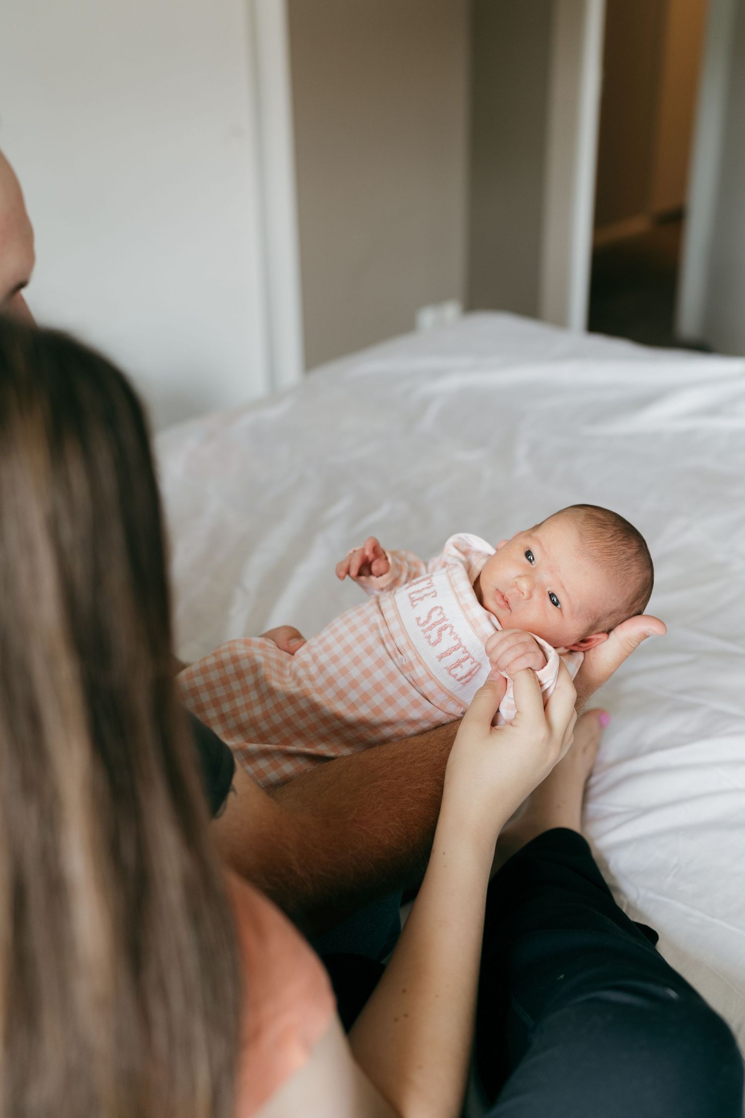 Baby in checkered outfit being held during indoor lifestyle photography session.