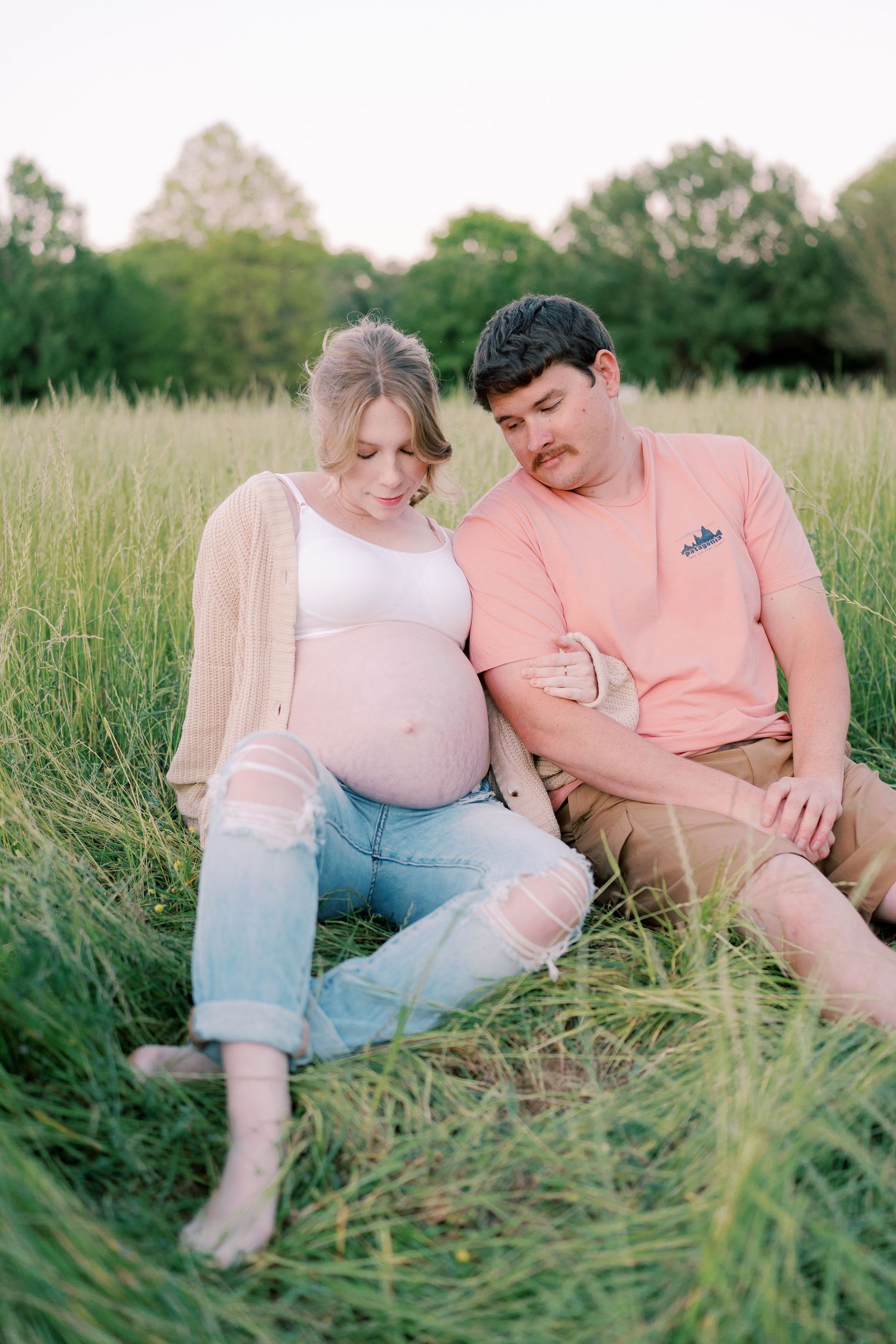 Couple relaxing together in a grassy field wearing coordinating pink and white outfits.