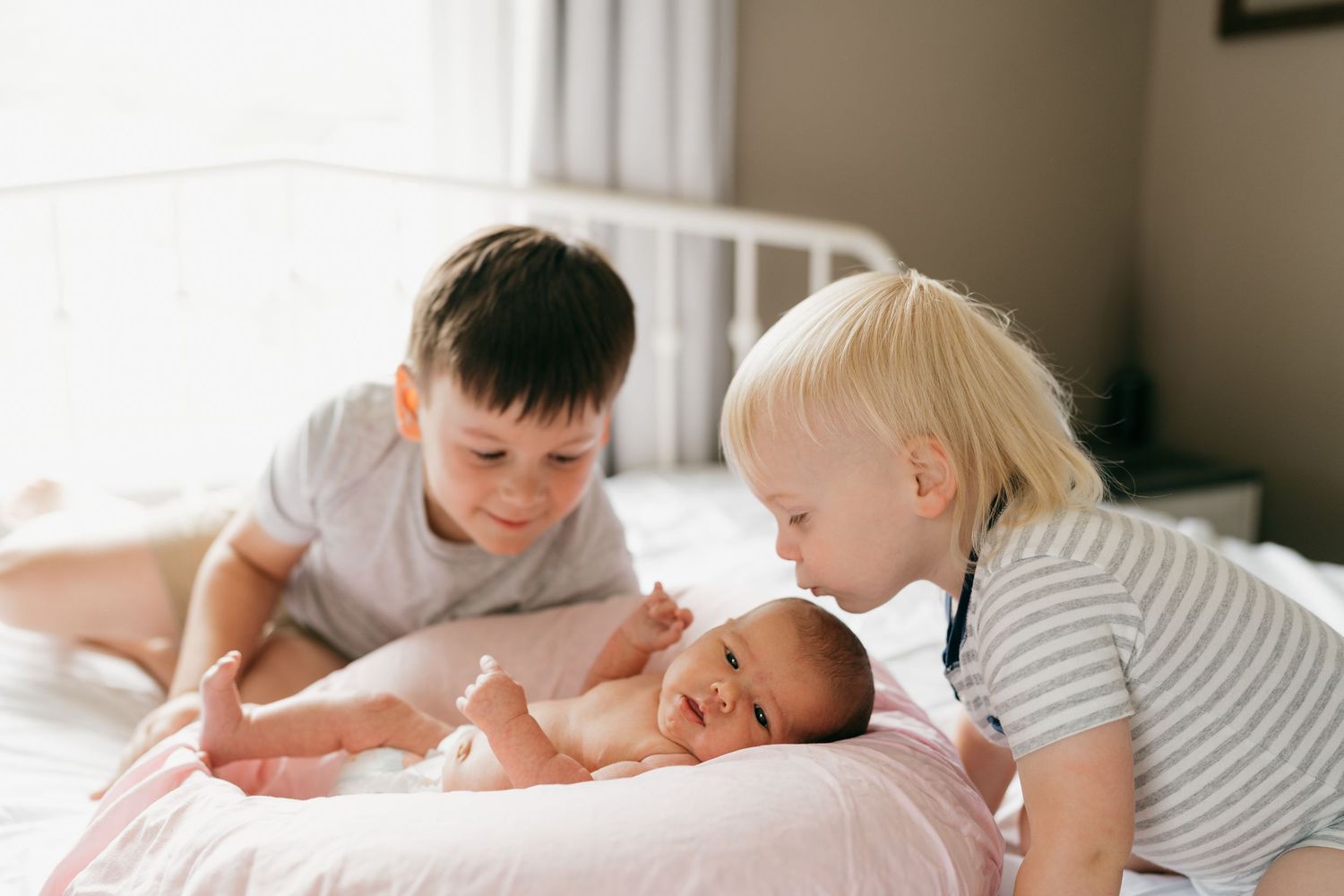 Siblings bonding with new baby on cozy bed in natural indoor setting.