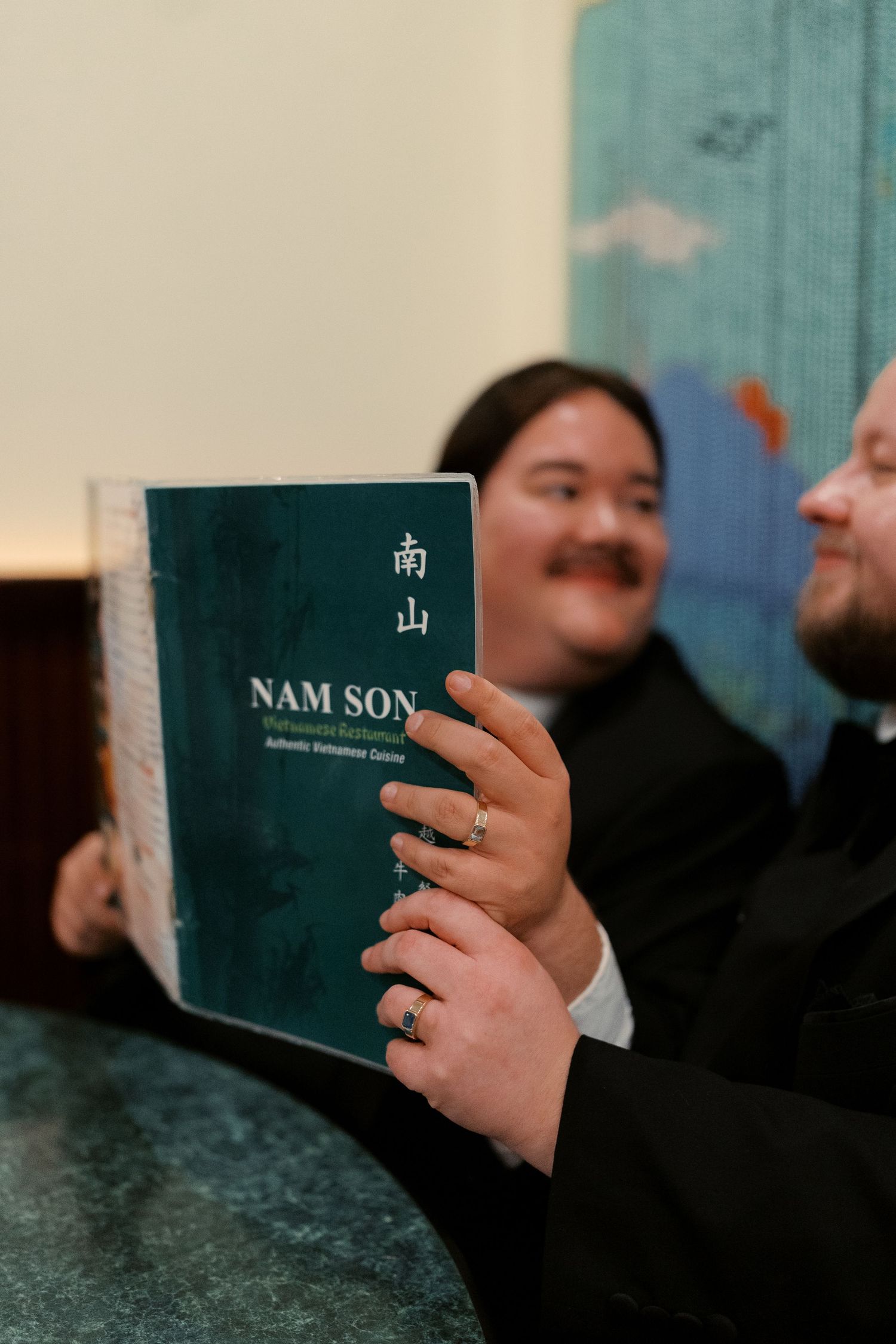 Hand holding a Nam Son restaurant menu against a blue-green background.