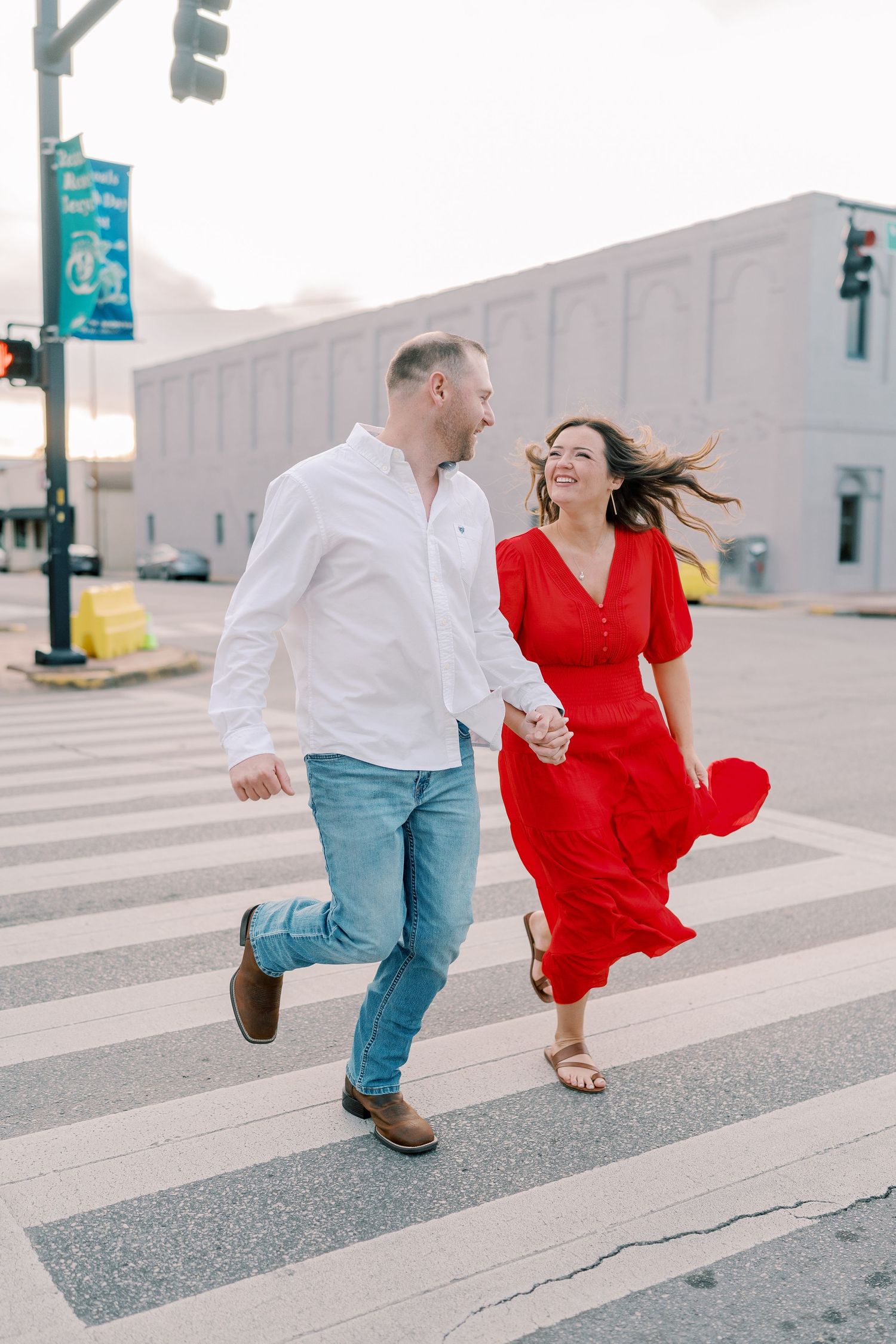 Playful couple runs and dances together across a crosswalk in urban setting.